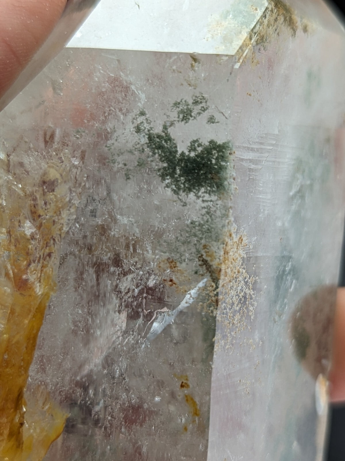 A translucent quartz crystal with green and yellow inclusions, featuring a natural, faceted cut.