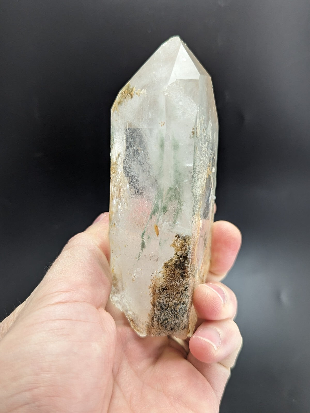 A translucent, clear quartz crystal with natural inclusions and earthy mineral deposits along its base.