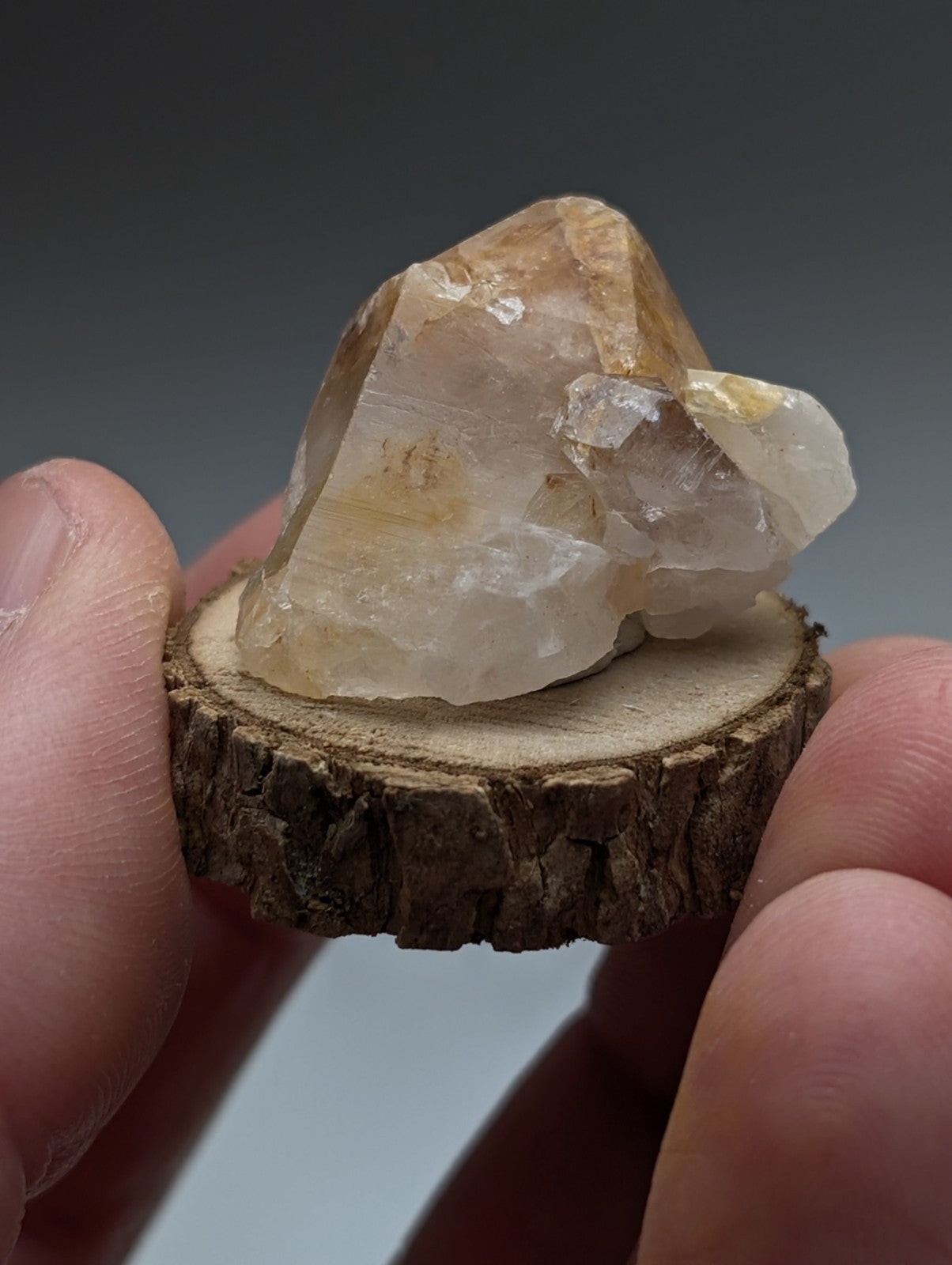 A clay-included quartz cluster with translucent amber hues and rough facets on a natural wood base from garland county arkansas