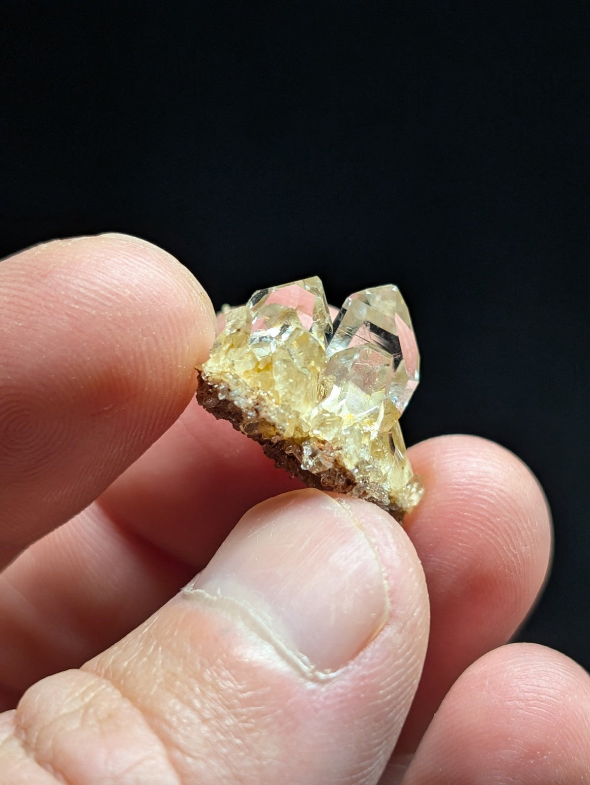 A translucent yellowish crystal cluster with clear, faceted points and a rough brown matrix base.