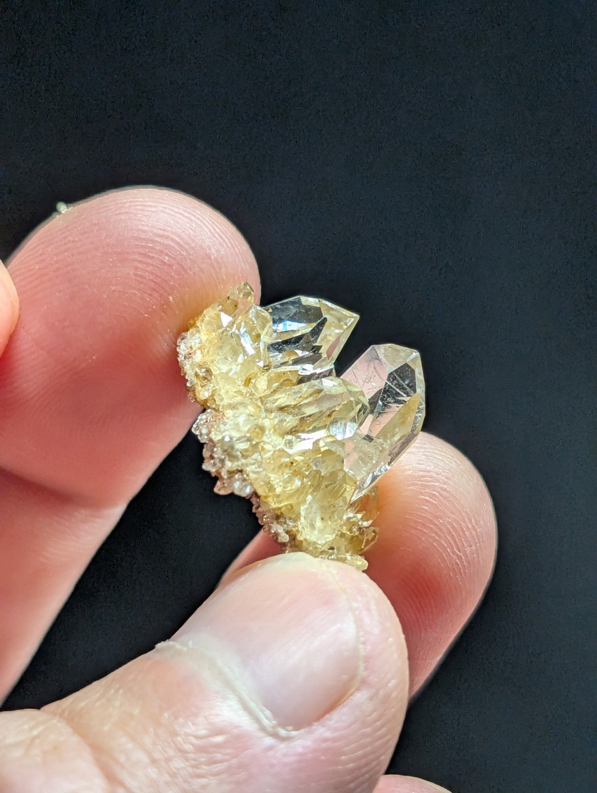A translucent yellow crystal cluster with sharp, faceted points and a rough, mineral-rich base.