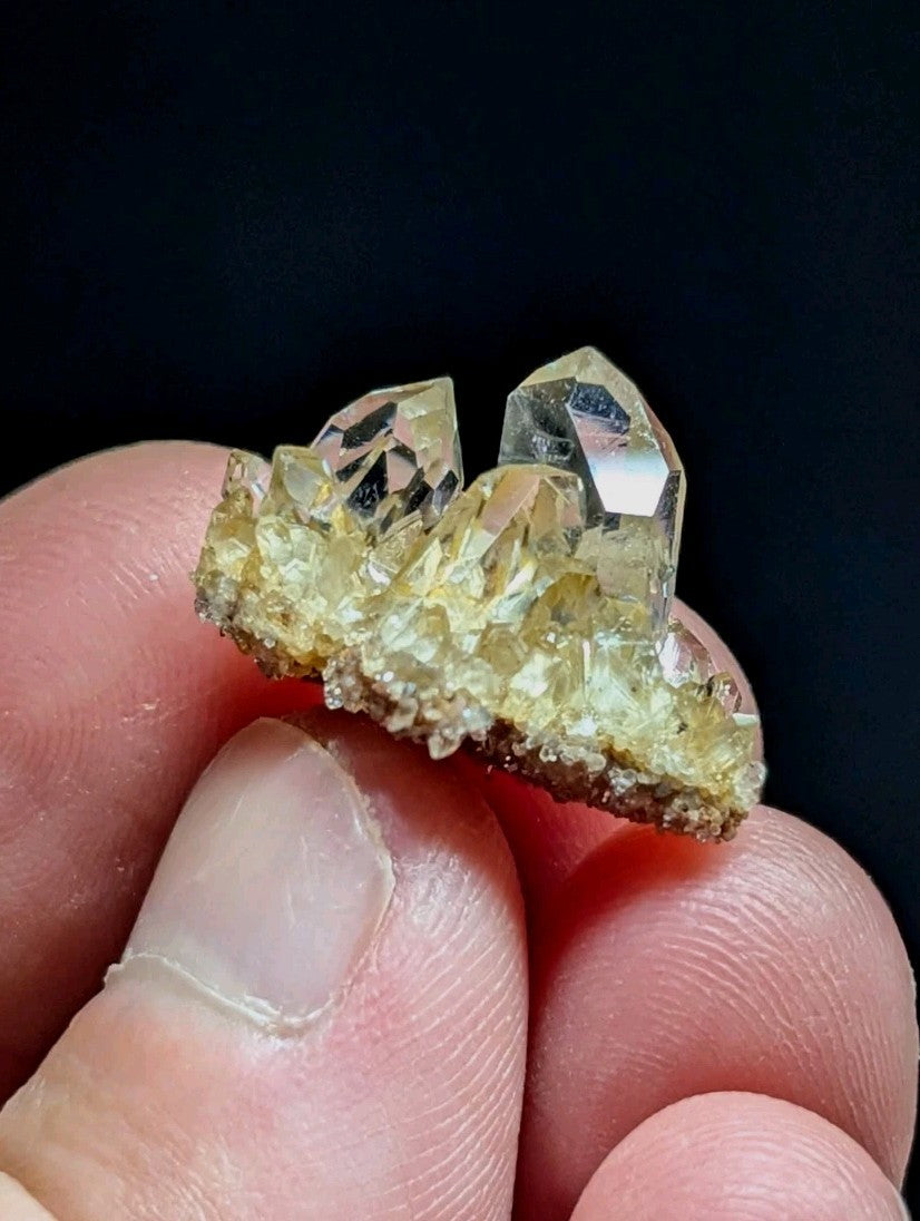 A cluster of translucent, pale yellow quartz crystals with sharp facets and a rough, earthy base.