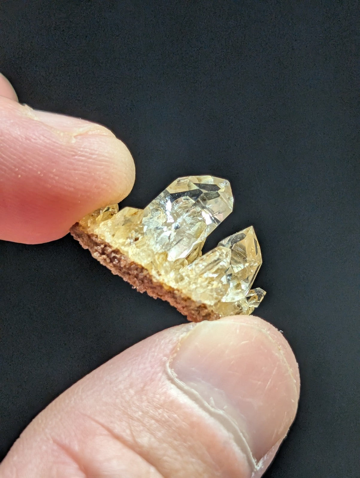 A translucent golden-yellow crystal cluster with sharp, faceted points emerging from a rough brown base.