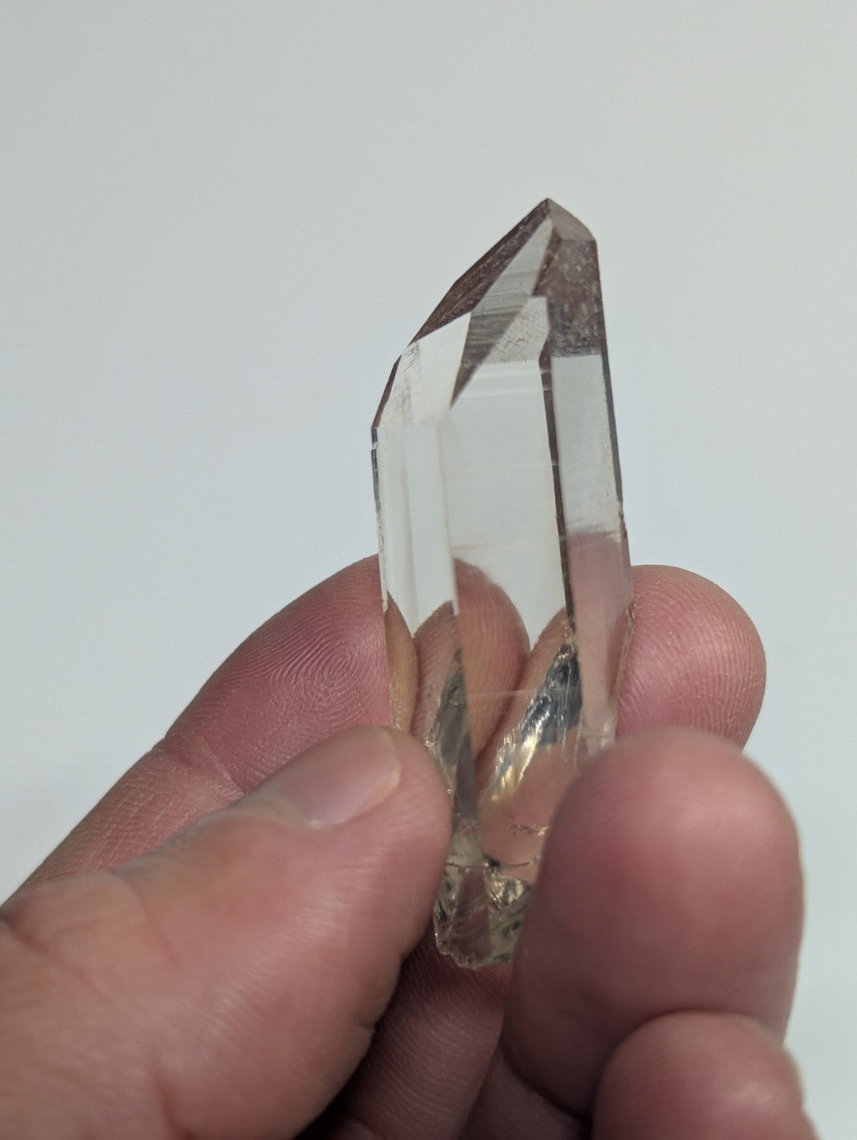 A clear, faceted quartz crystal with a pointed tip and natural inclusions.