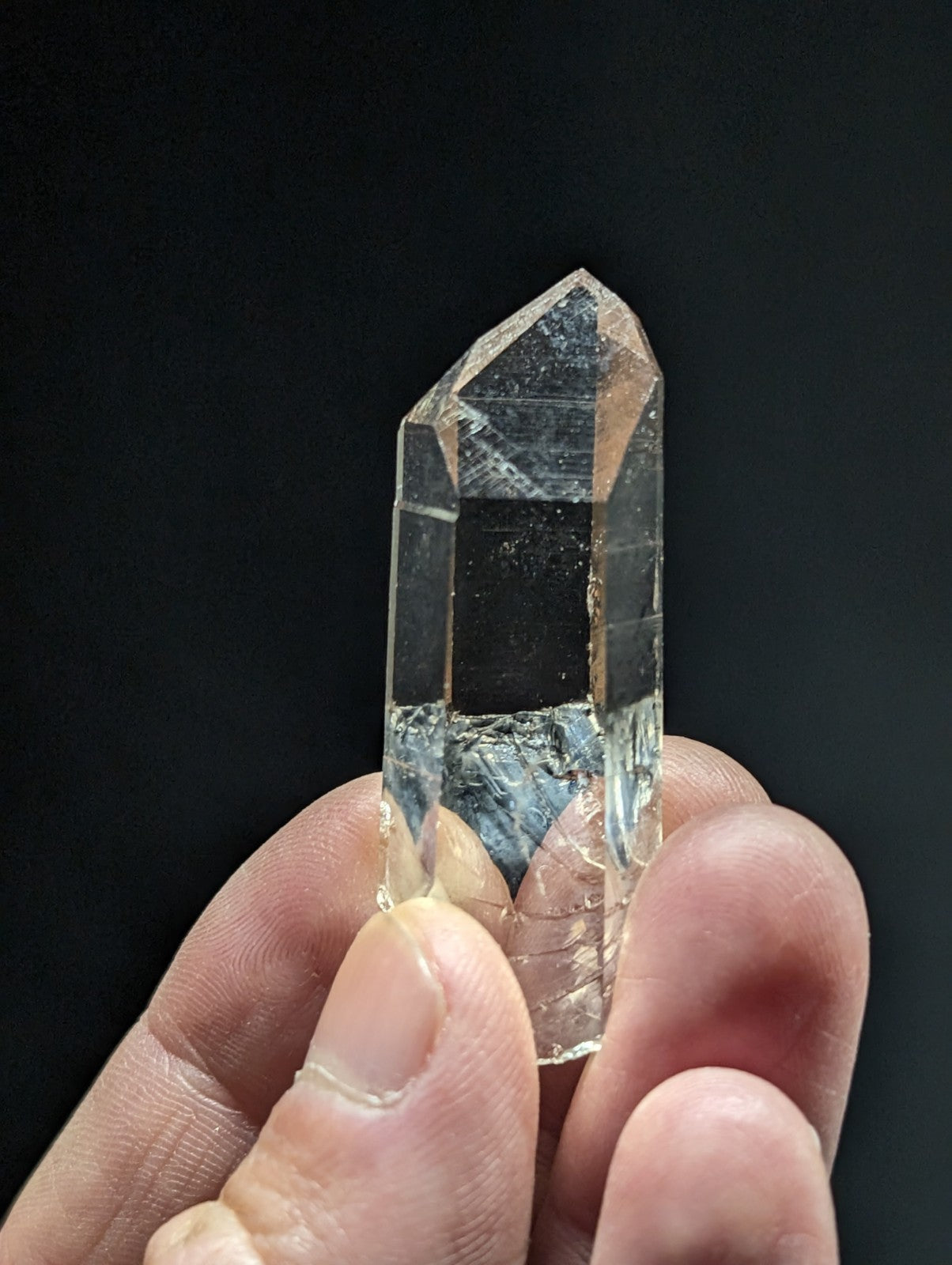 A clear, faceted quartz crystal with a pointed tip and visible internal inclusions.