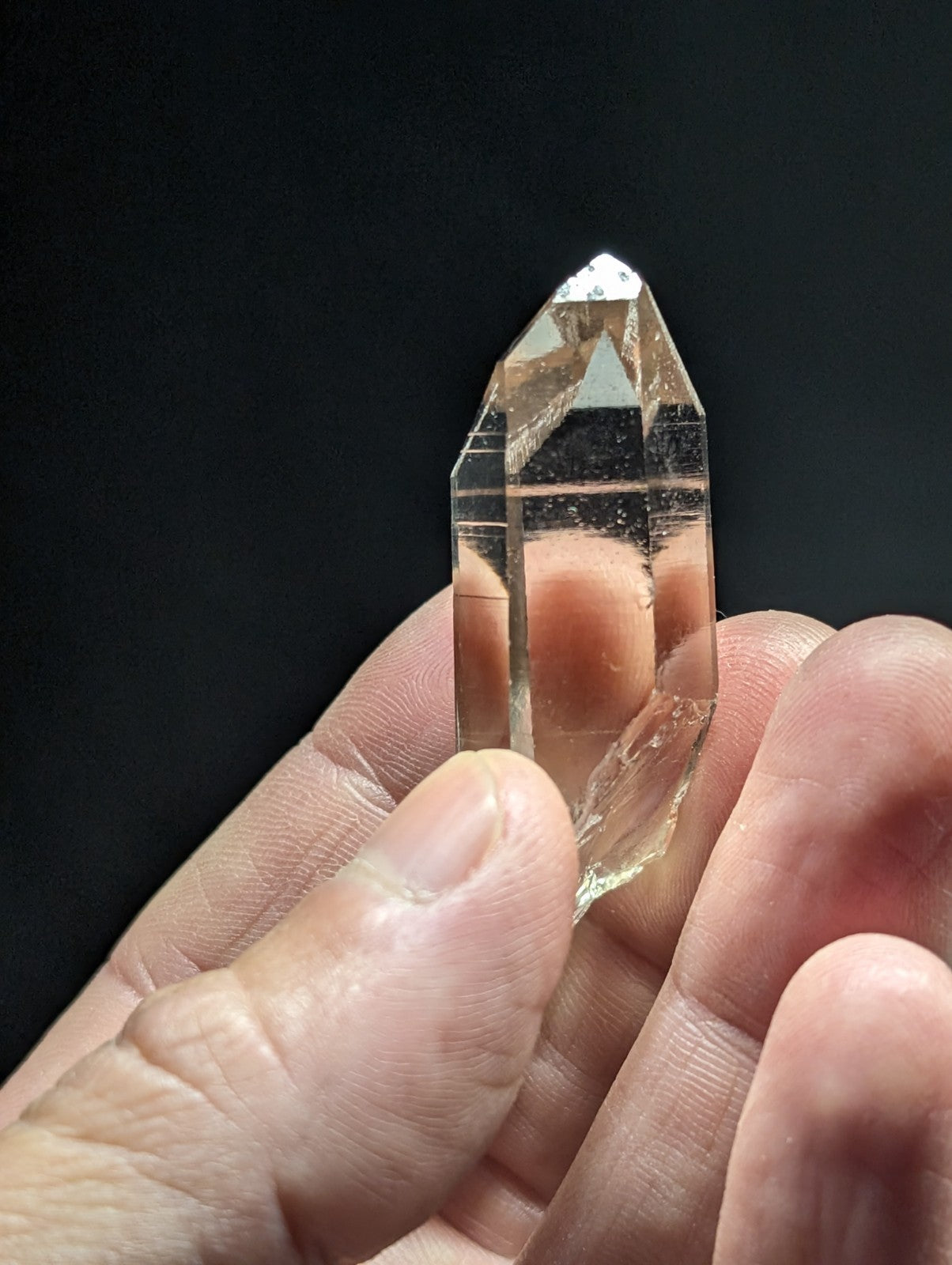 A clear, faceted quartz crystal held gently in a hand.