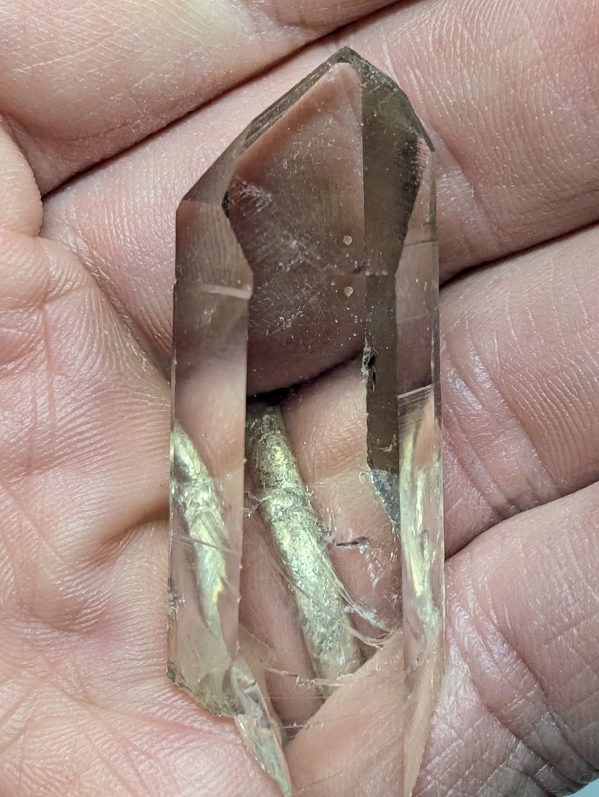 A translucent brown crystal with a pointed top and visible internal inclusions, held gently in an open palm.