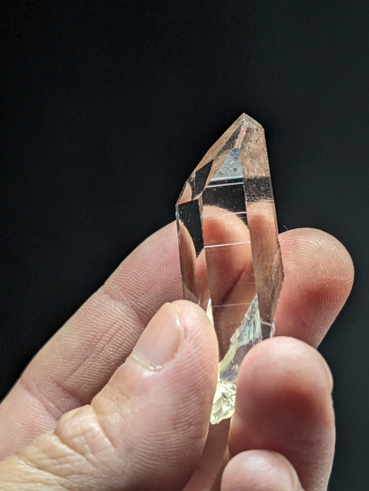A translucent, faceted quartz crystal with a pointed tip and subtle golden hue.
