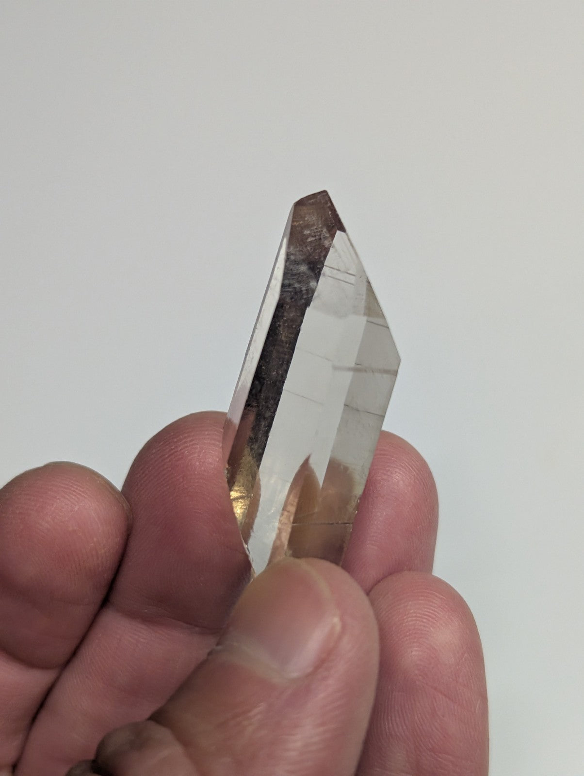 A clear quartz crystal with a pointed tip and natural inclusions, held gently between fingers.