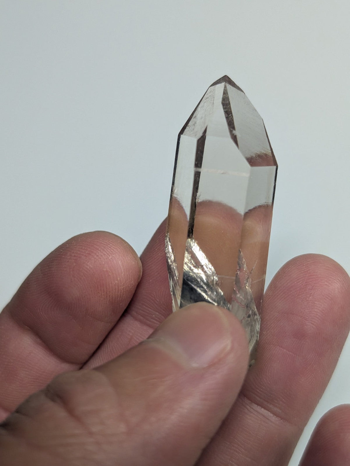 A clear, faceted quartz crystal with a pointed tip and natural internal inclusions.
