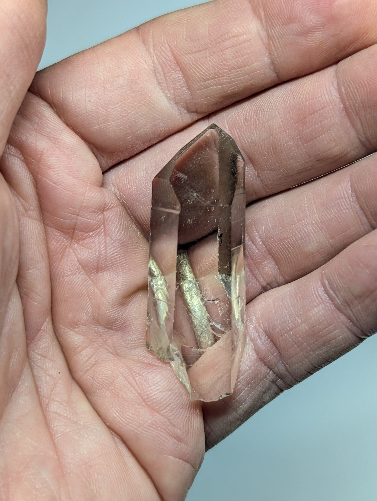 A translucent smoky quartz crystal with a pointed tip and visible internal inclusions, held gently in an open palm.