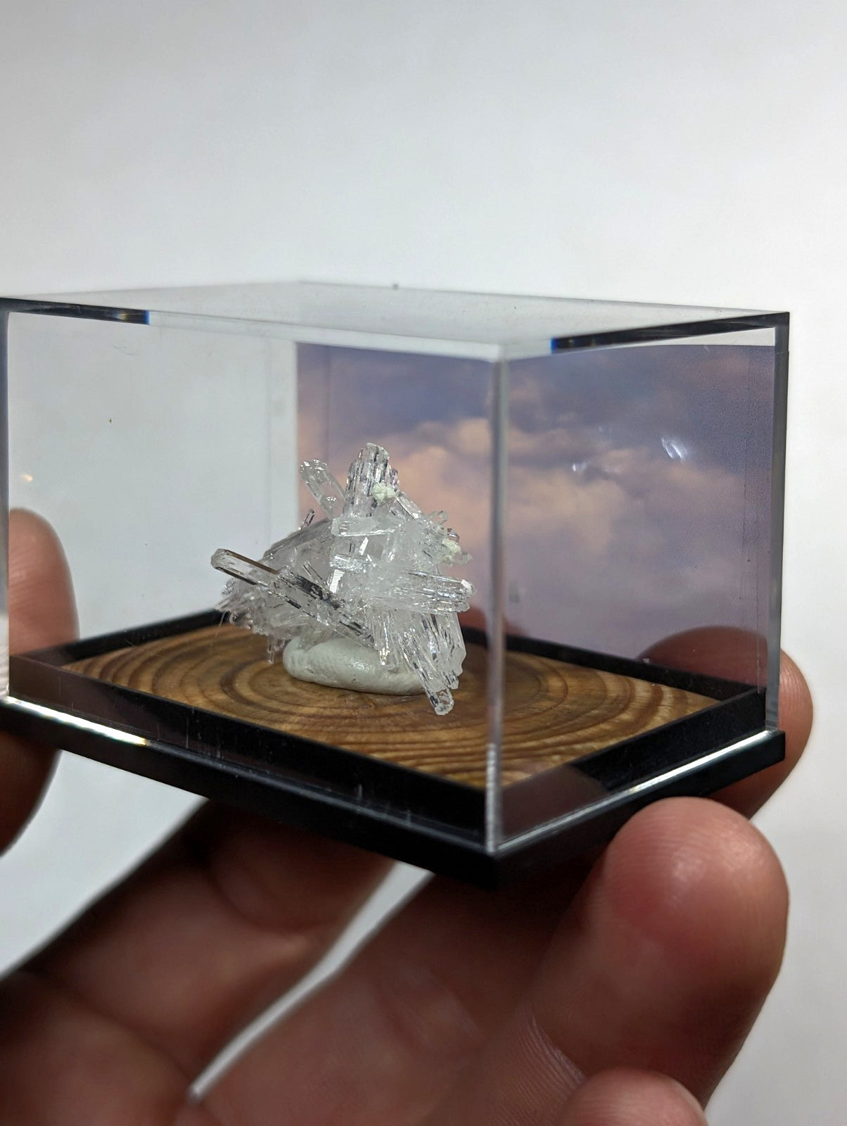 A clear, faceted crystal cluster displayed in a transparent acrylic display case with a wooden base.