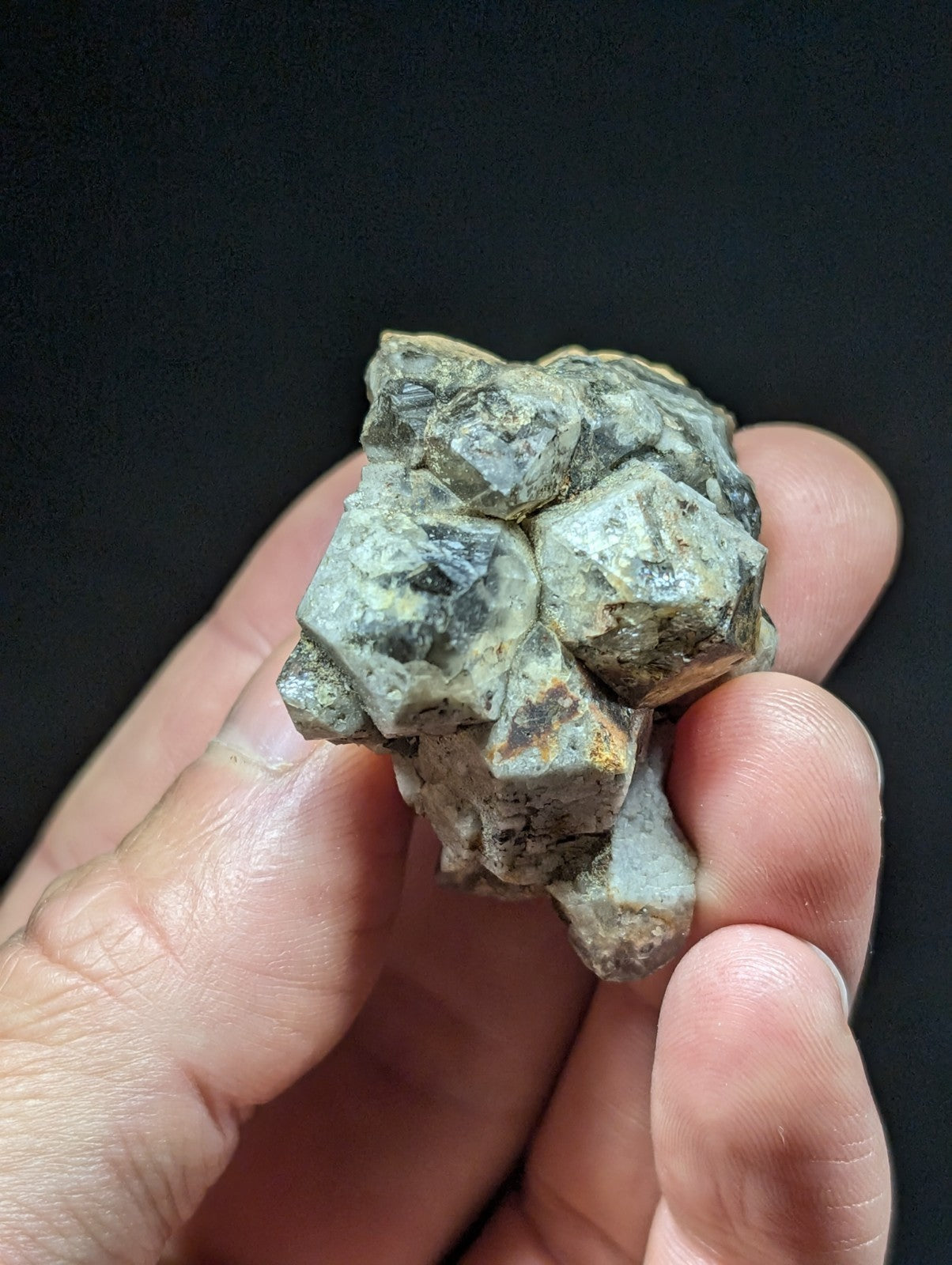 A rough, irregularly shaped mineral specimen with a mottled green and gray surface, featuring patches of dark veining and subtle orange-brown discoloration.