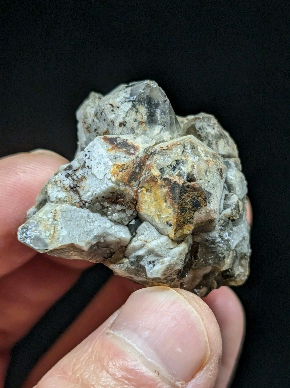 A rough, clustered mineral specimen with translucent gray crystals and patches of yellowish-brown oxidation.