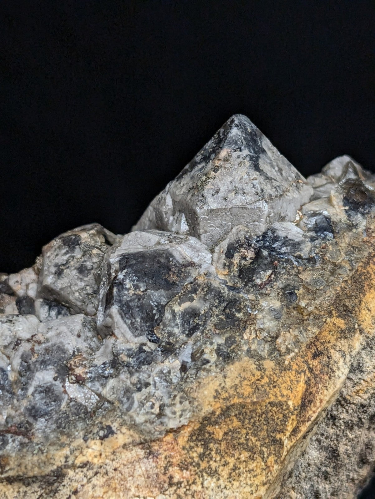 A cluster of translucent gray quartz crystals with sharp, pointed tips growing from a rugged, earth-toned rock base.