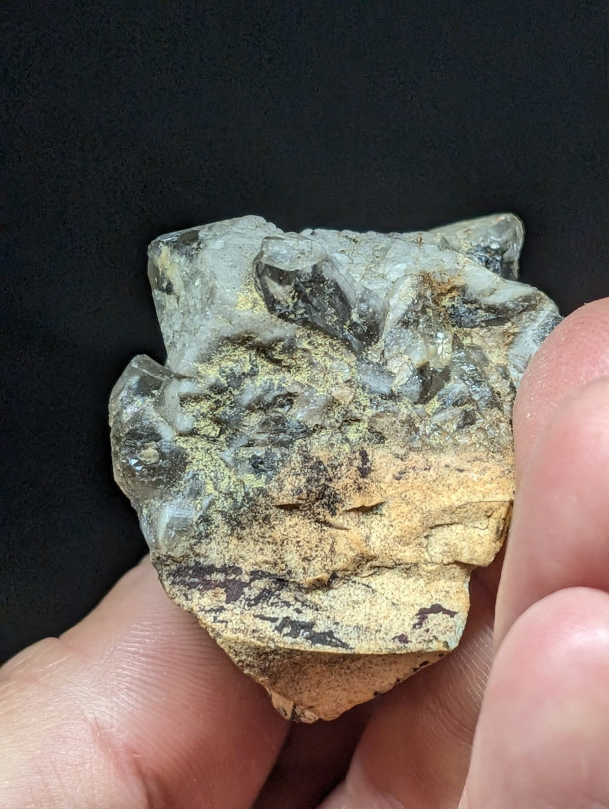 A rough, irregularly shaped stone with a mottled surface of gray, greenish hues and patches of yellow-brown.