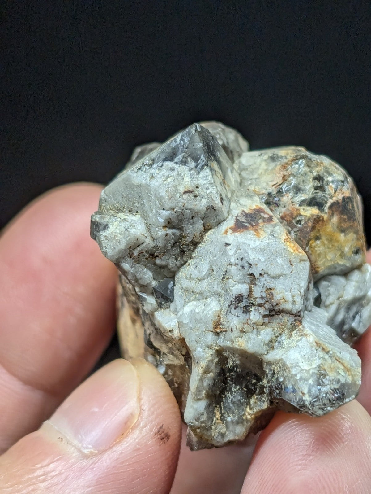 A rough, grayish-white mineral specimen with jagged edges and patches of brown and yellow oxidation.