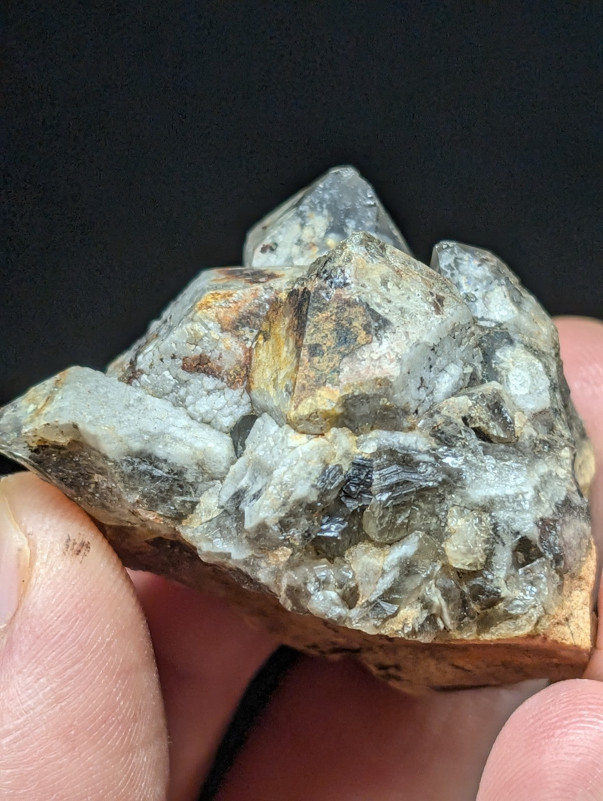 A cluster of translucent gray quartz crystals with speckles of brown and black, embedded in a rough, earthy matrix.