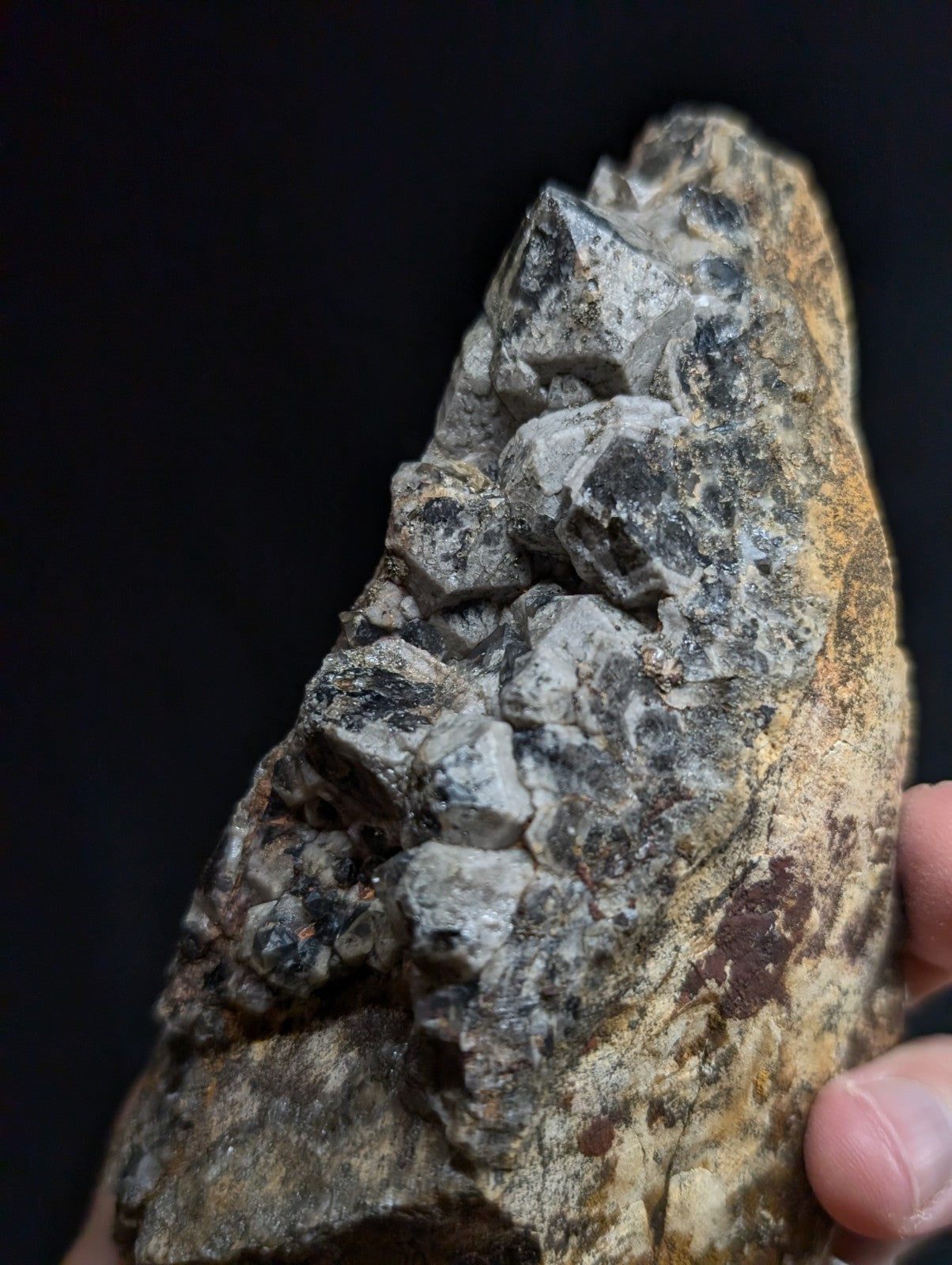 A rugged, naturally occurring mineral specimen featuring a cluster of grayish-white crystals growing from a rougher, earth-toned matrix.