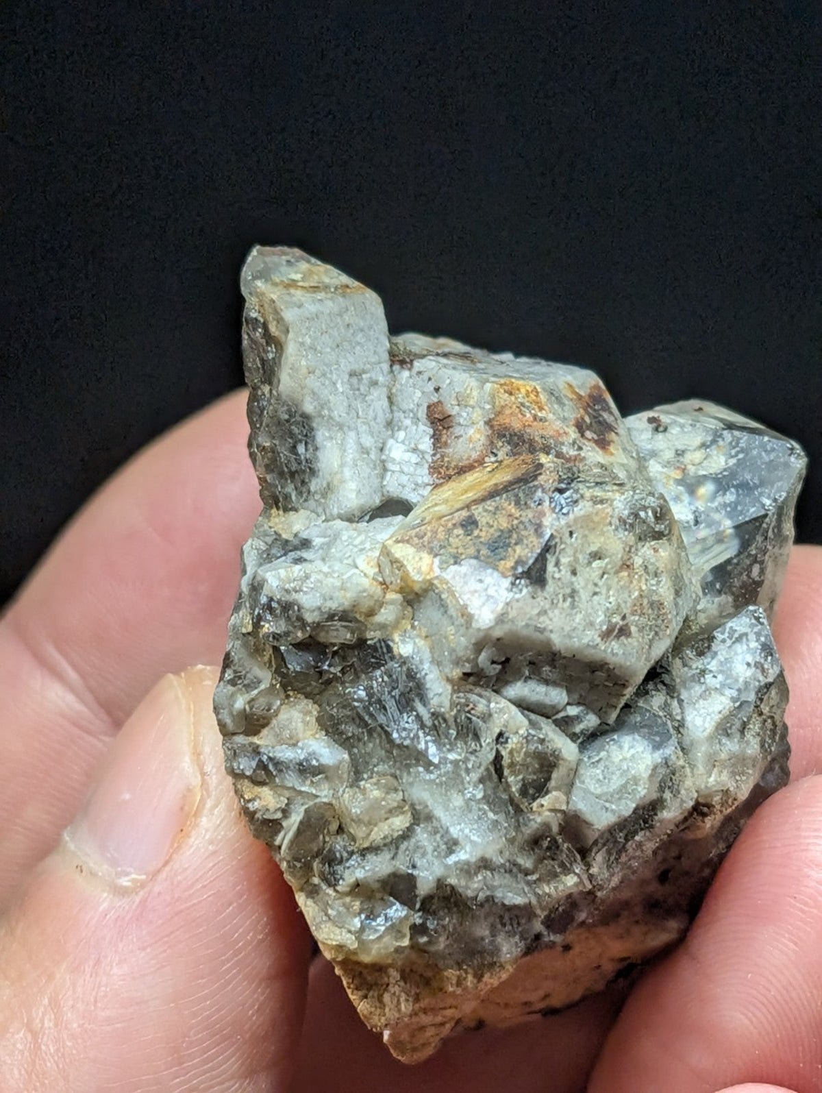 A rough, grayish-green mineral specimen with crystalline facets and earthy brown patches.