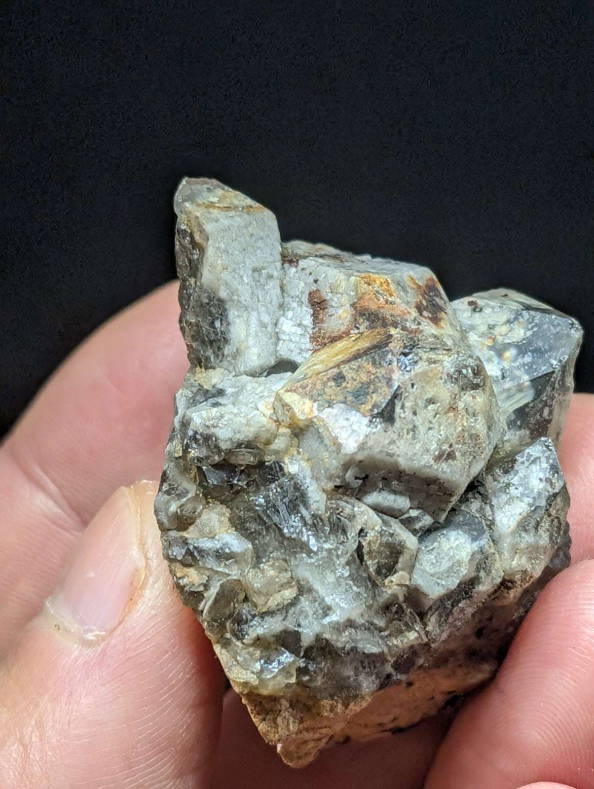 A rough, grayish-green mineral specimen with crystalline facets and earthy brown patches.