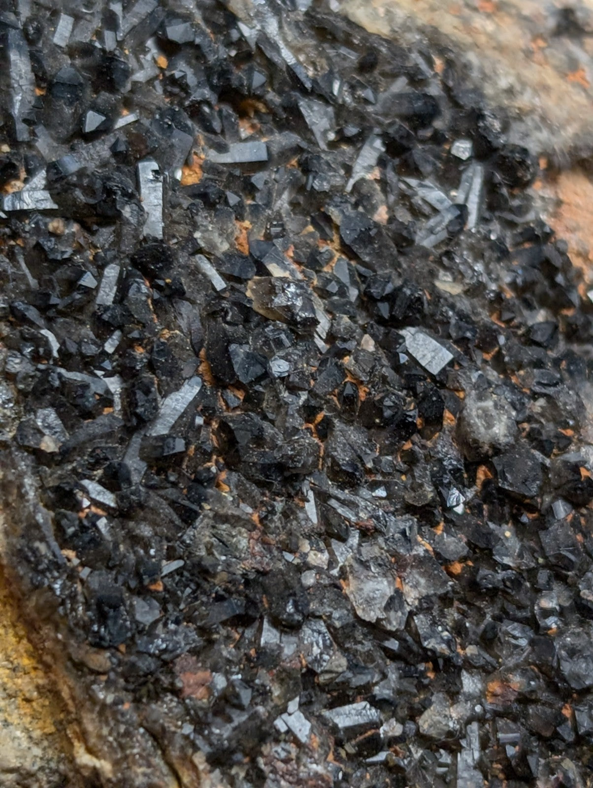 A cluster of dark, angular crystals with metallic sheen and subtle orange mineral inclusions.