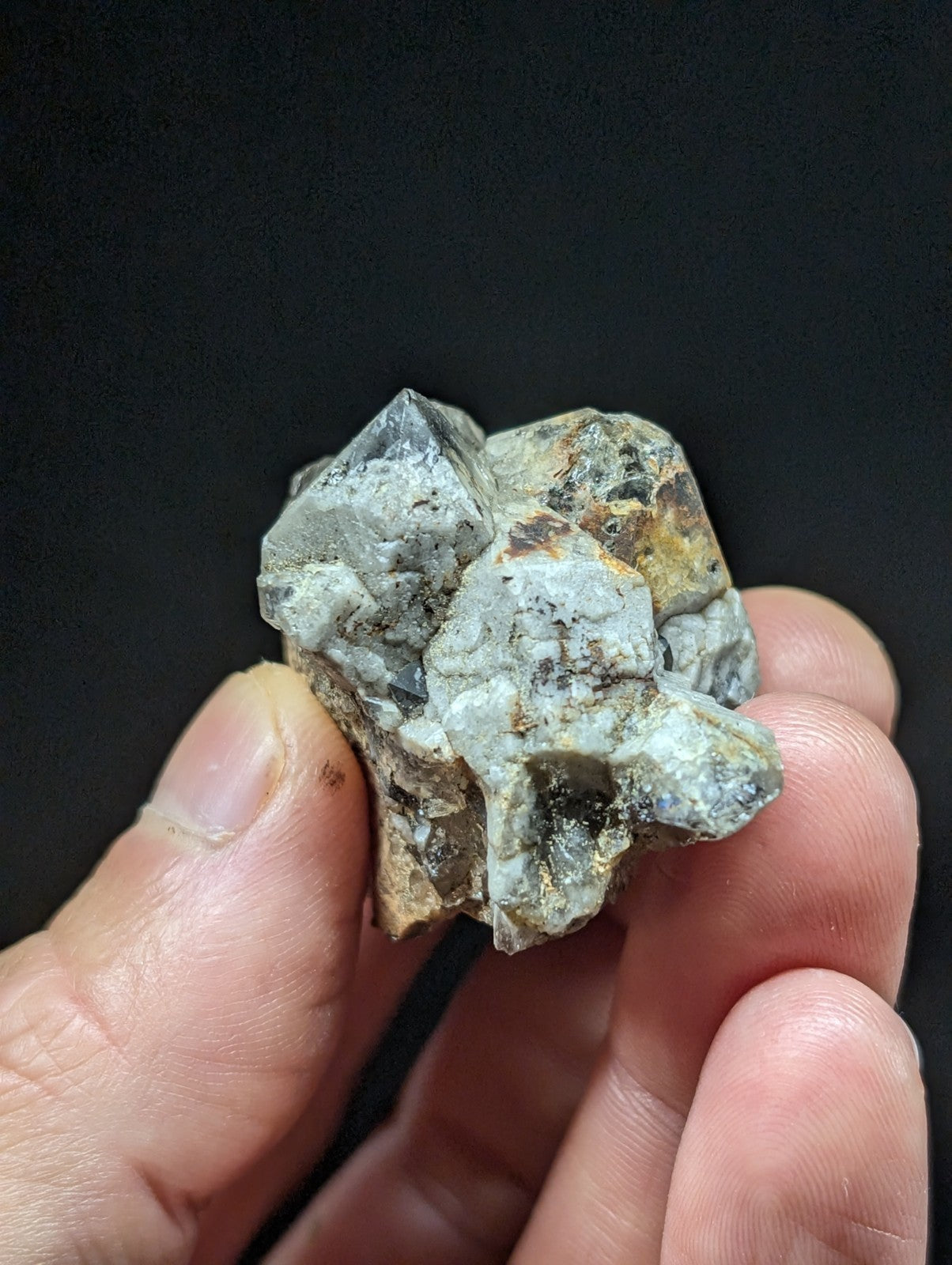 A rough, clustered mineral specimen with translucent gray crystals and earthy brownish-yellow patches.