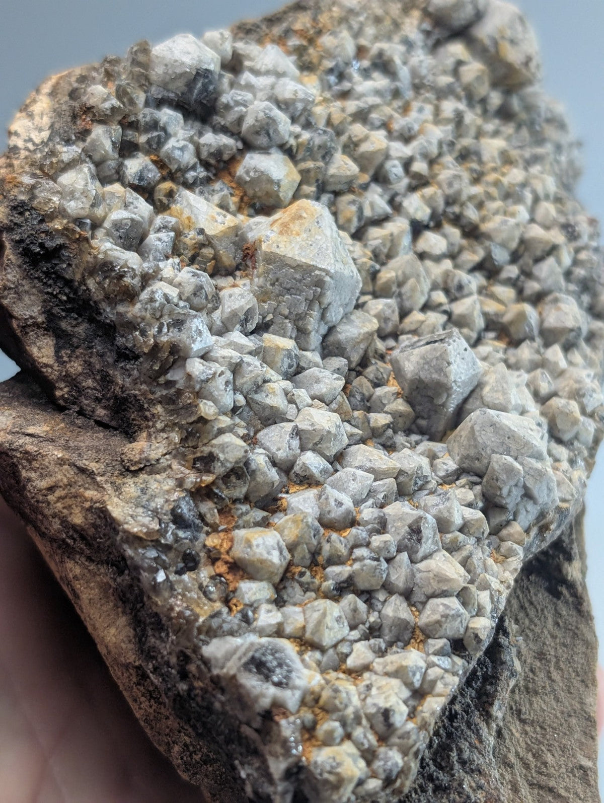 A rugged, grayish-white mineral specimen featuring a dense cluster of angular crystals growing from a darker, earthy matrix.