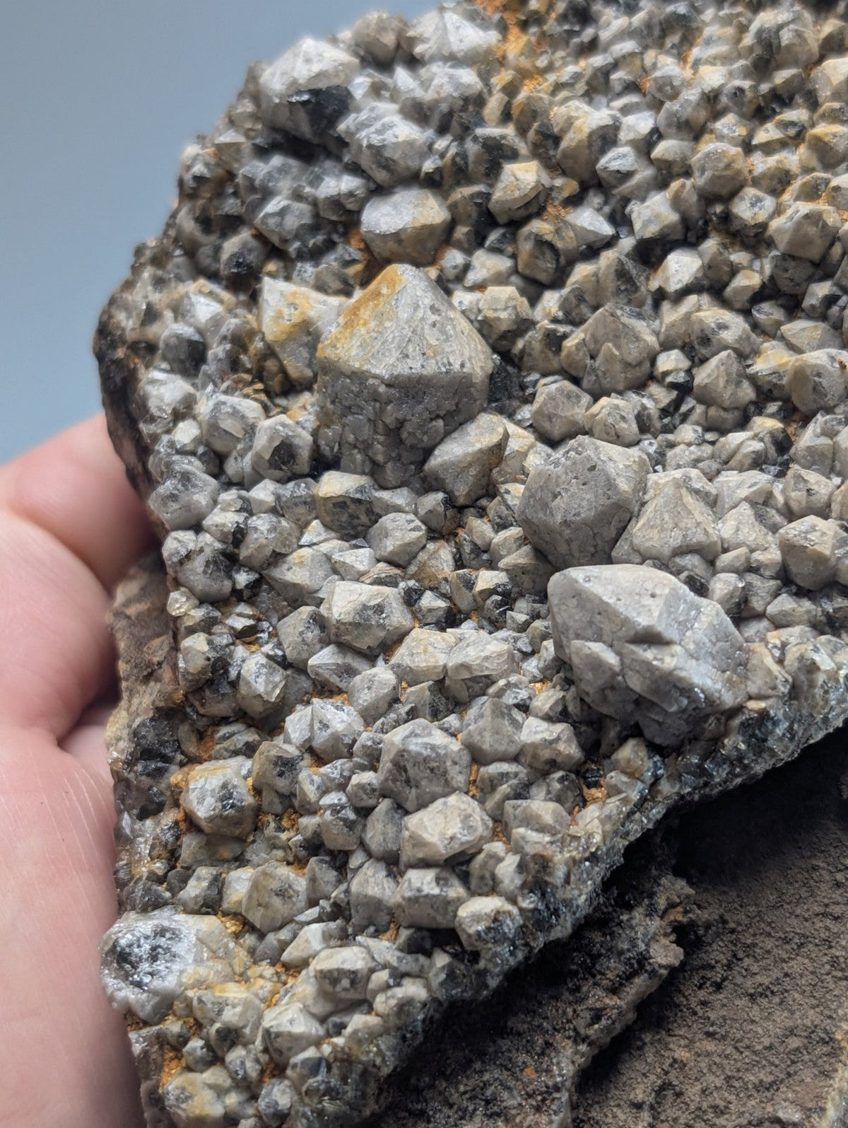 A gray, textured mineral specimen featuring a dense cluster of small, angular crystals with subtle hints of yellow and black veining.