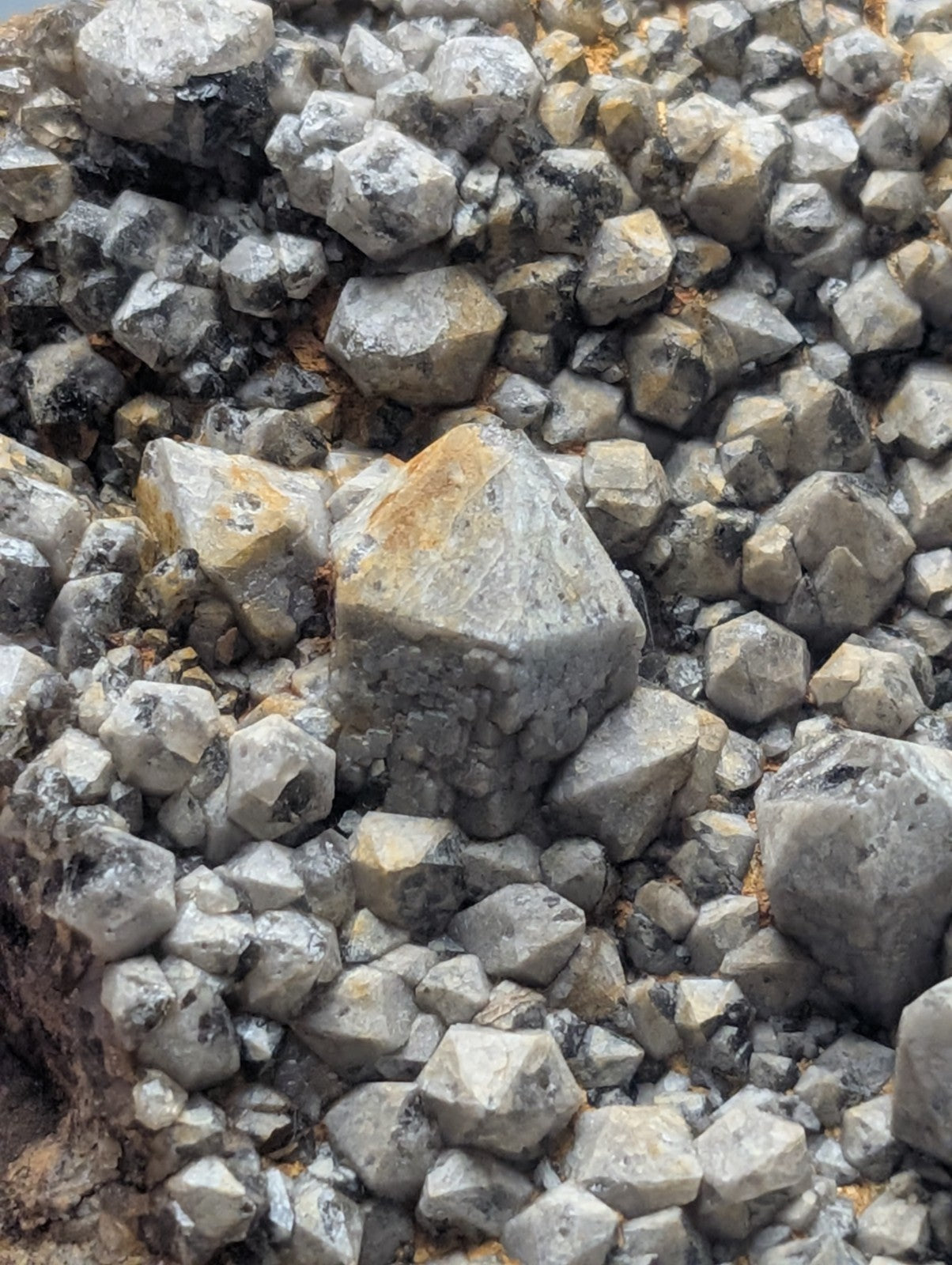 A cluster of gray, faceted mineral crystals with some exhibiting yellowish and dark streaks.