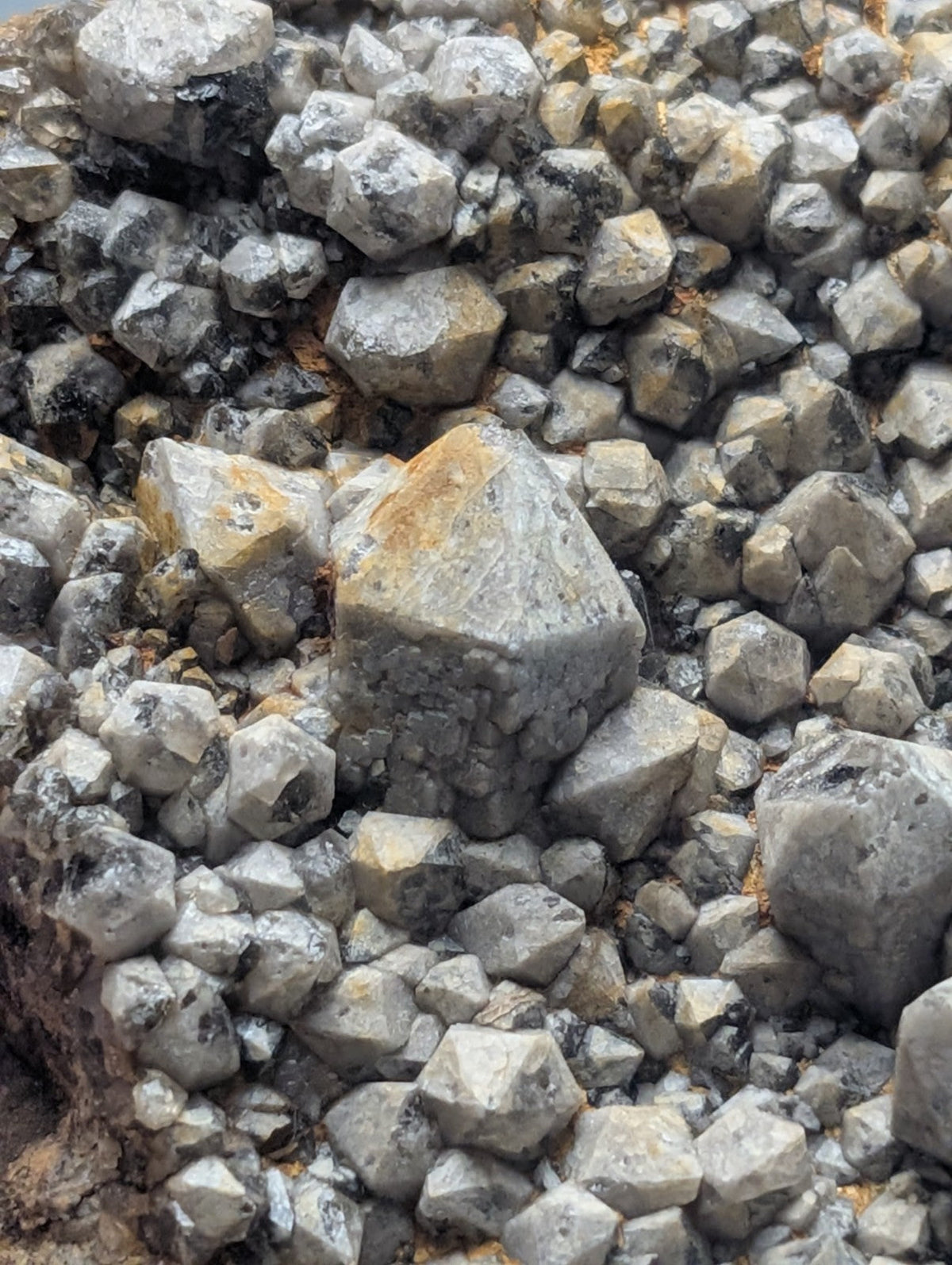 A cluster of gray, faceted mineral crystals with some exhibiting yellowish and dark streaks.