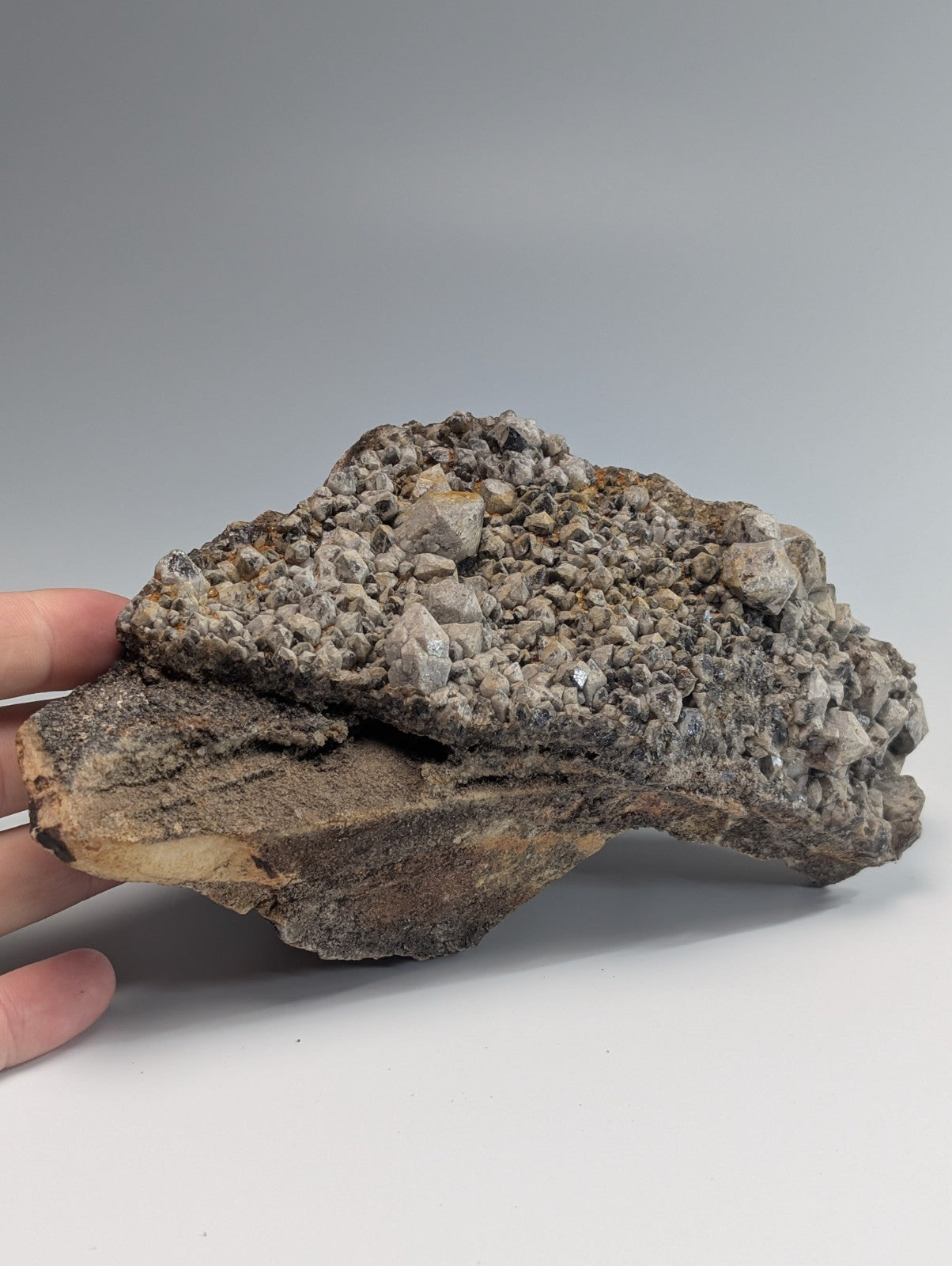 A rugged, grayish-brown mineral specimen with a textured surface featuring clusters of small, crystalline formations.