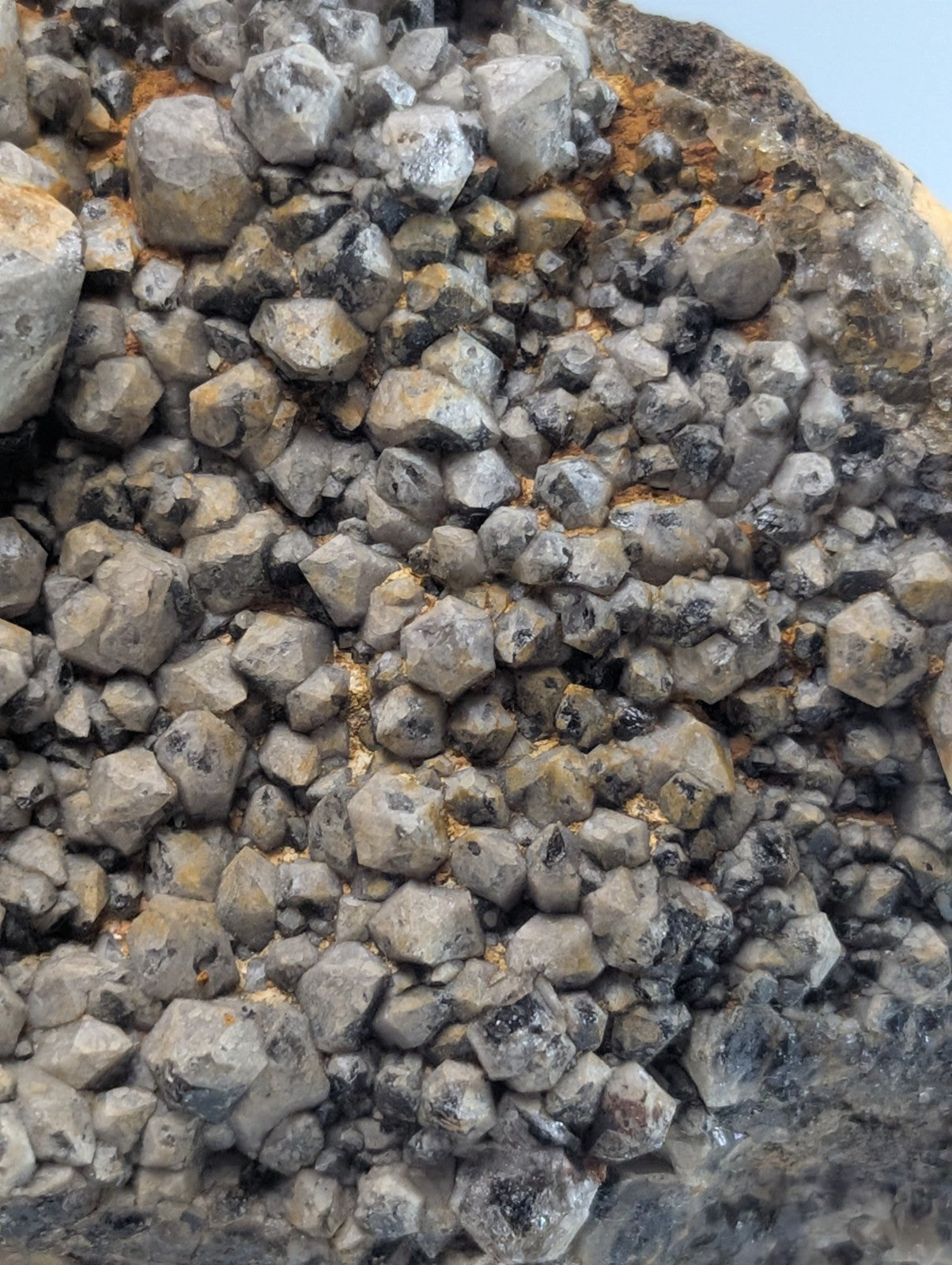 A cluster of gray, faceted quartz crystals growing densely from a dark rock matrix.