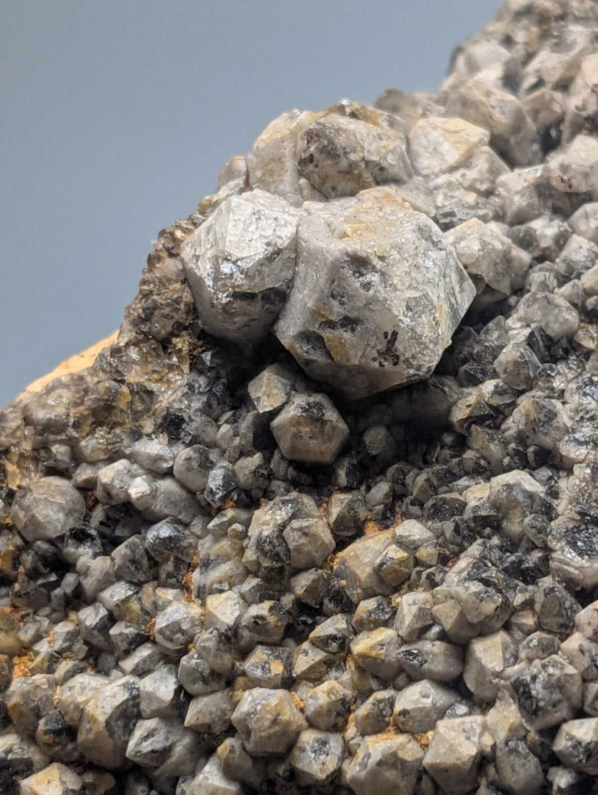 A cluster of gray, faceted mineral crystals with some exhibiting a metallic sheen and others displaying dark inclusions.
