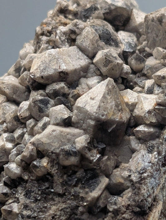 A cluster of gray, faceted quartz crystals with dark inclusions.