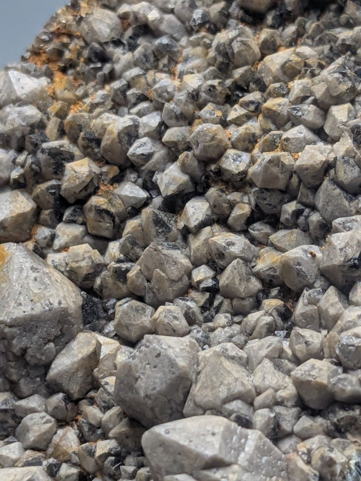 A dense cluster of gray, angular mineral crystals with speckles of black and hints of orange oxidation.