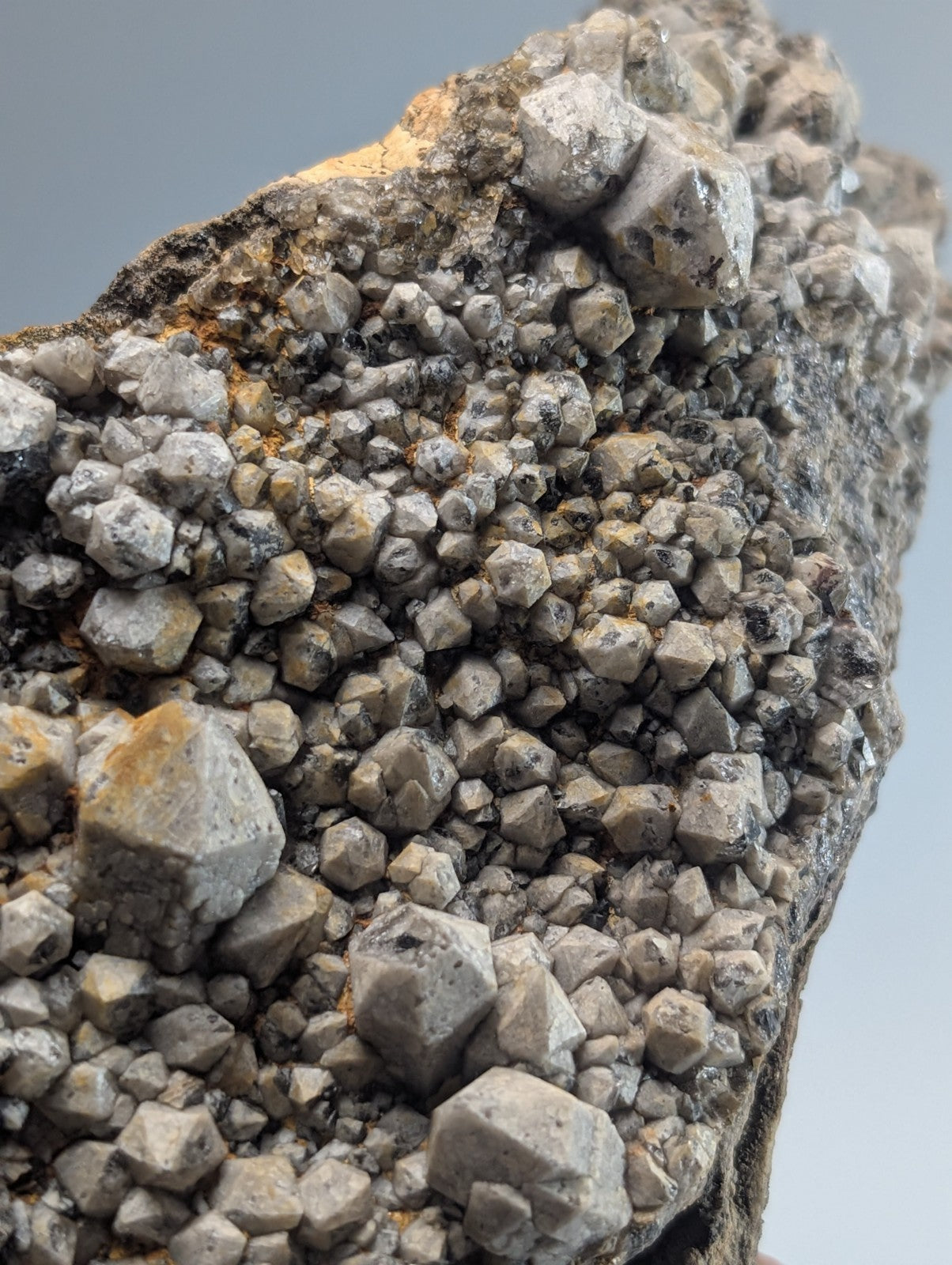 A gray, crystalline mineral specimen with a dense cluster of angular, faceted crystals growing from a darker rock matrix.