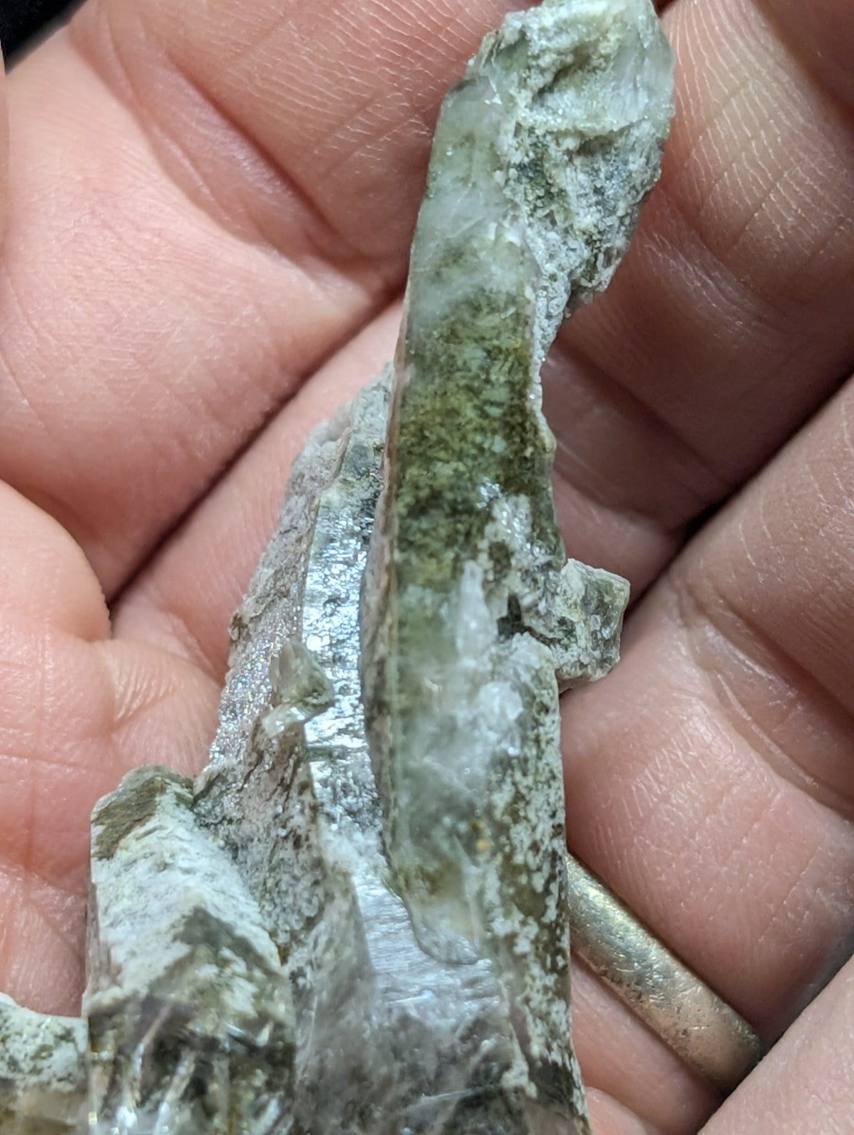 A translucent greenish crystal with a rough, jagged surface and visible mineral inclusions.