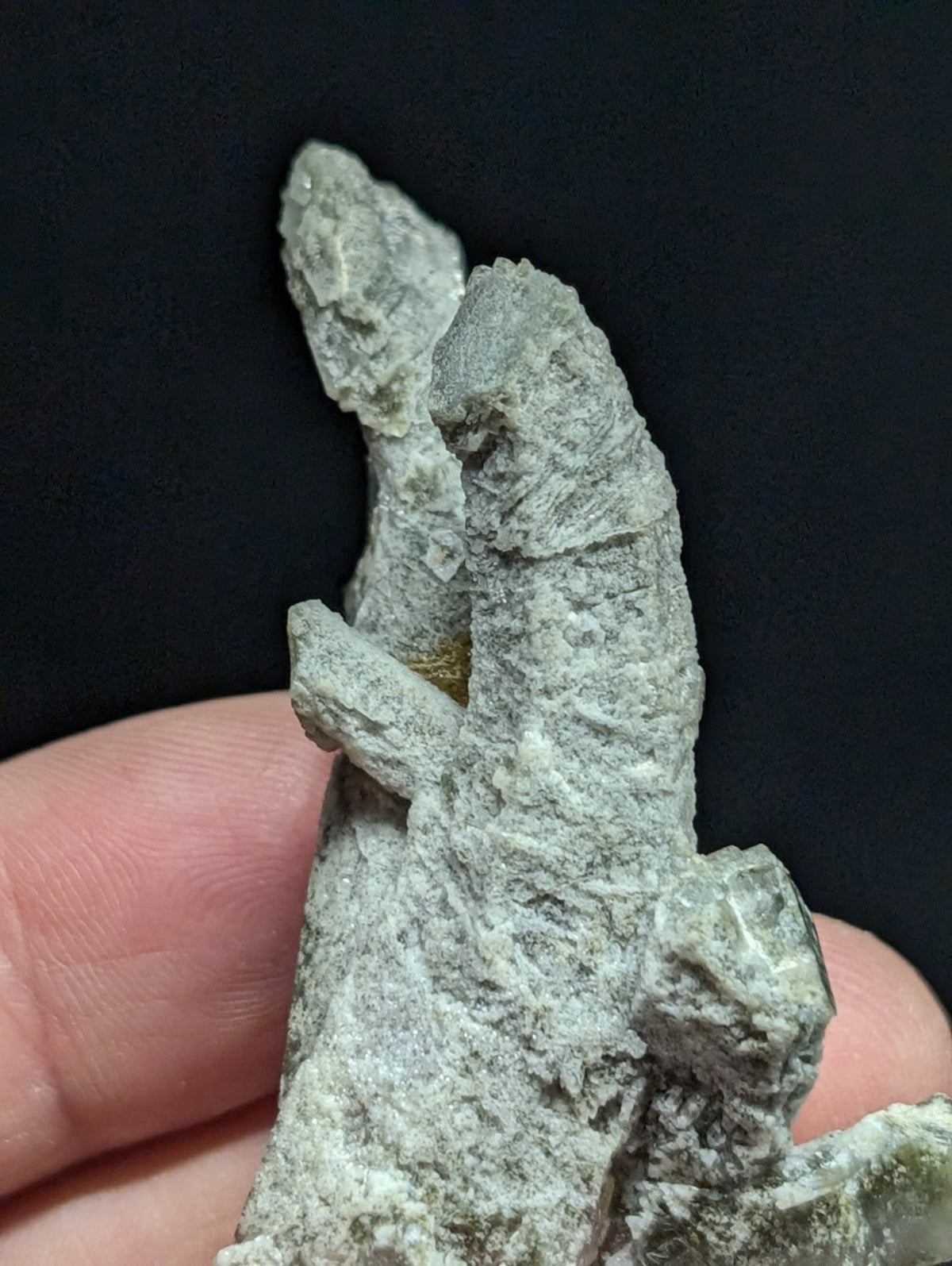 A textured, pale greenish-gray mineral specimen with a rough, crystalline surface and irregular formations.