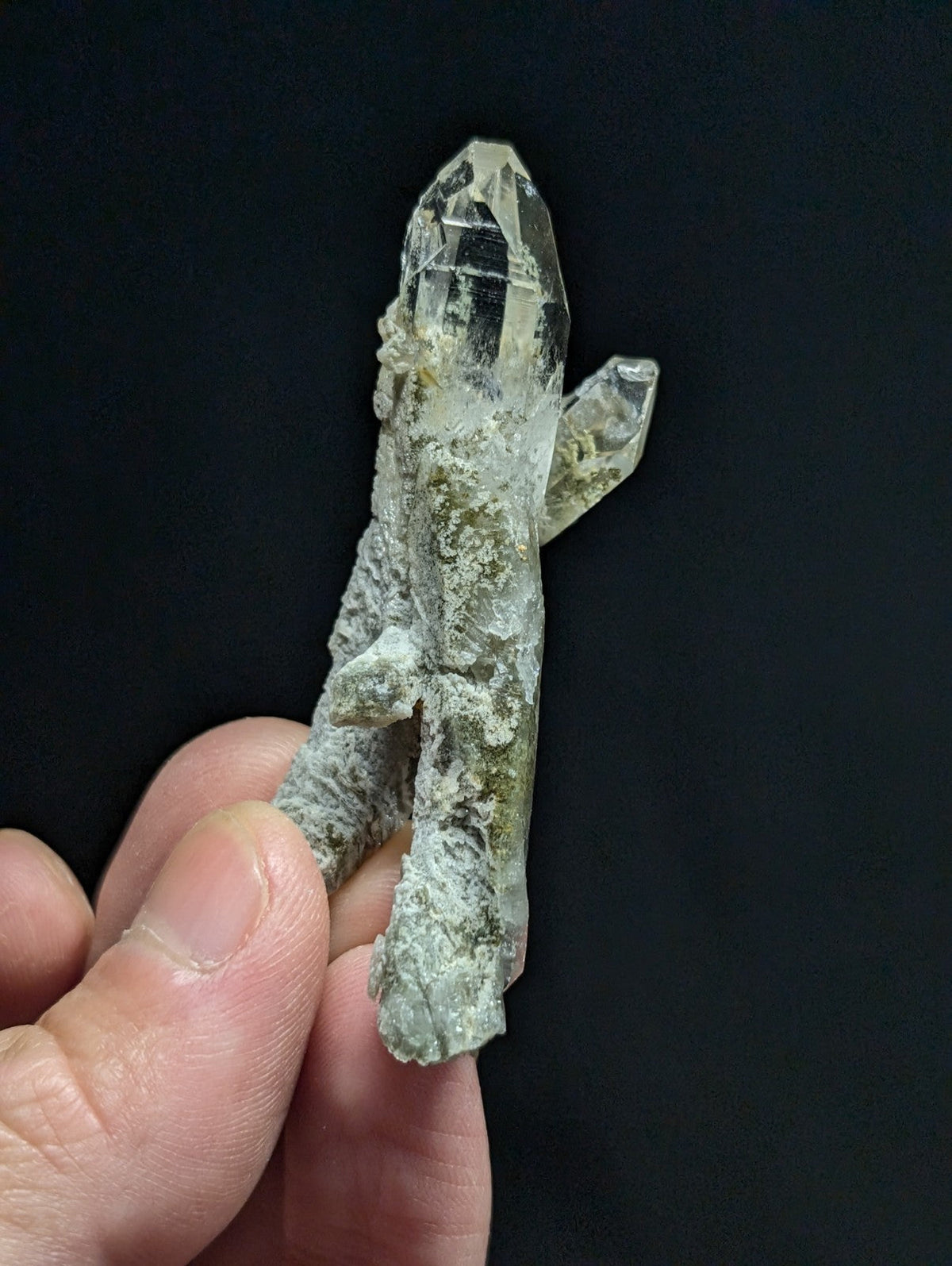 A translucent quartz crystal cluster with a clear, faceted top and greenish-gray matrix base.