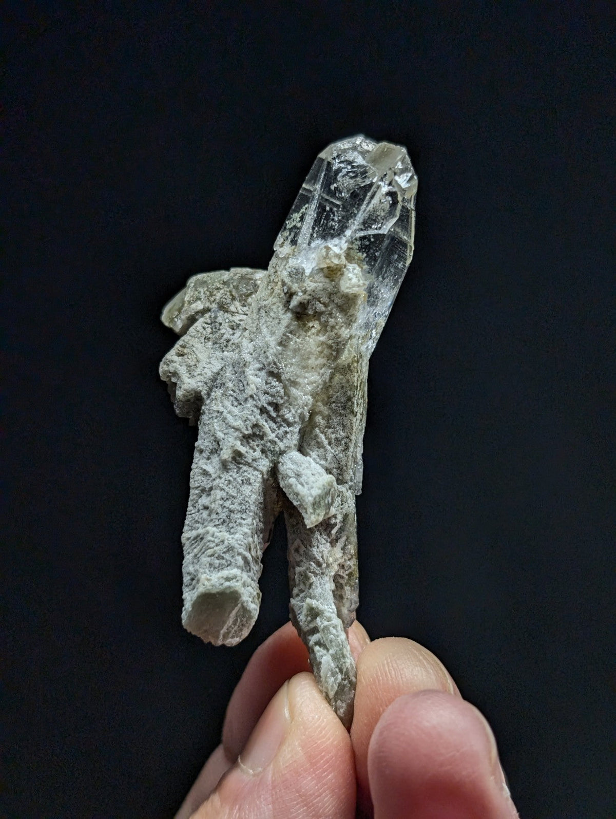 A translucent, clear quartz crystal with a rough, grayish matrix base and sharp, faceted points.