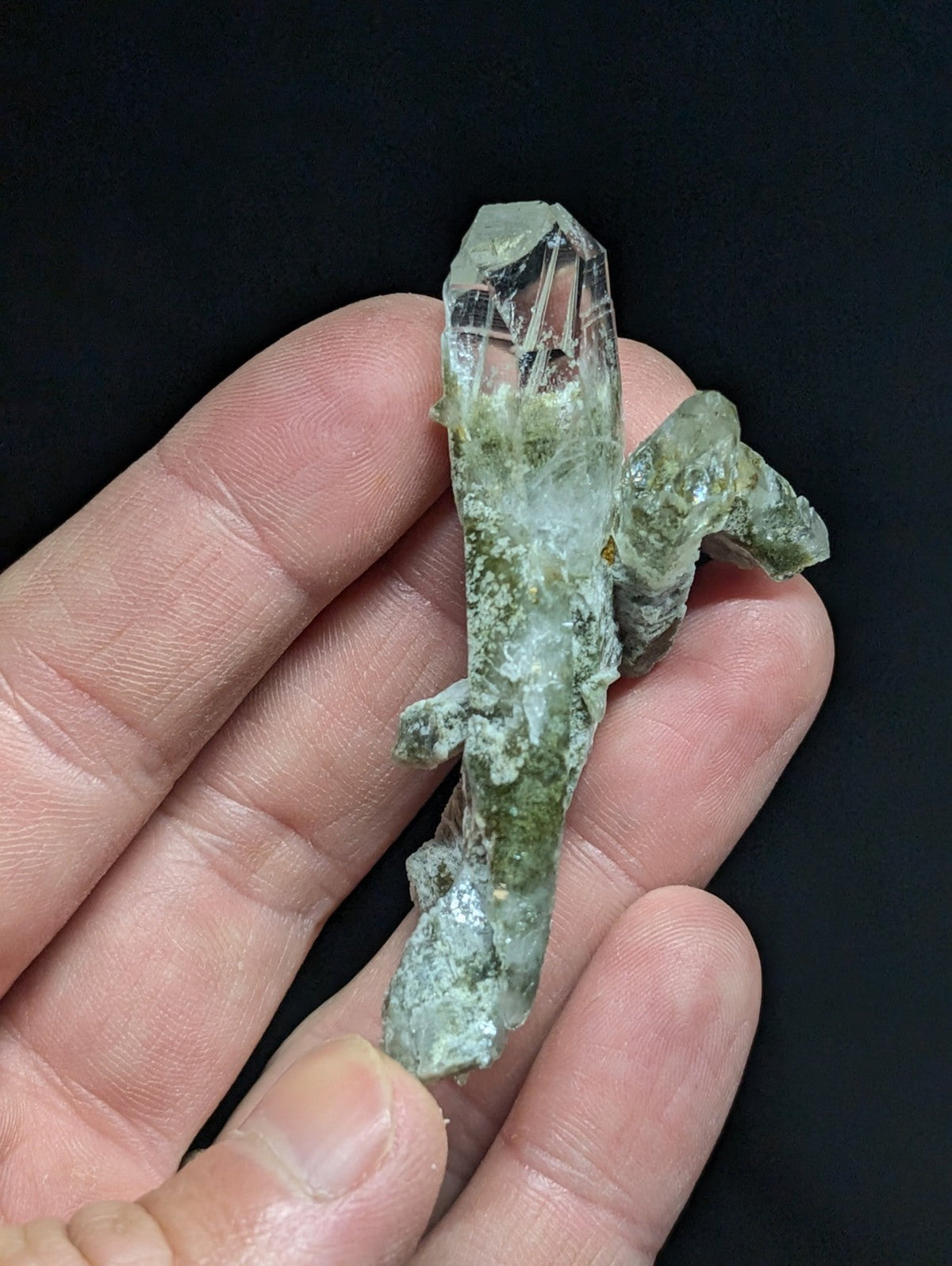 A translucent green crystal with a clear, faceted top and mossy-green base held in hand.
