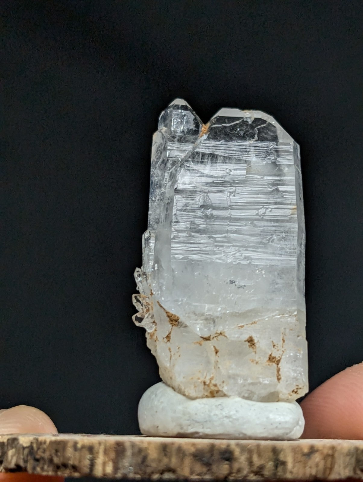 A translucent, clear quartz crystal with visible internal striations and a rough, natural base resting on a white pedestal.