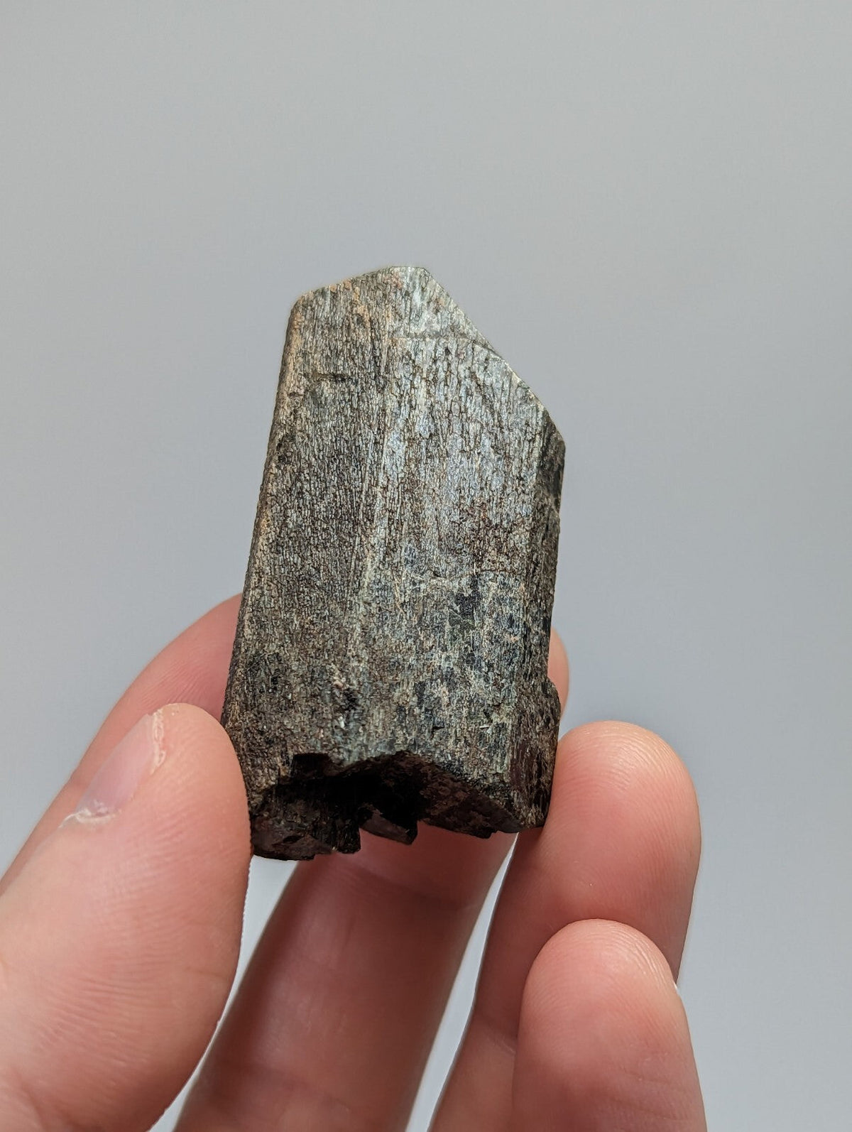 A rough, dark gray mineral specimen with a textured surface and angular facets.