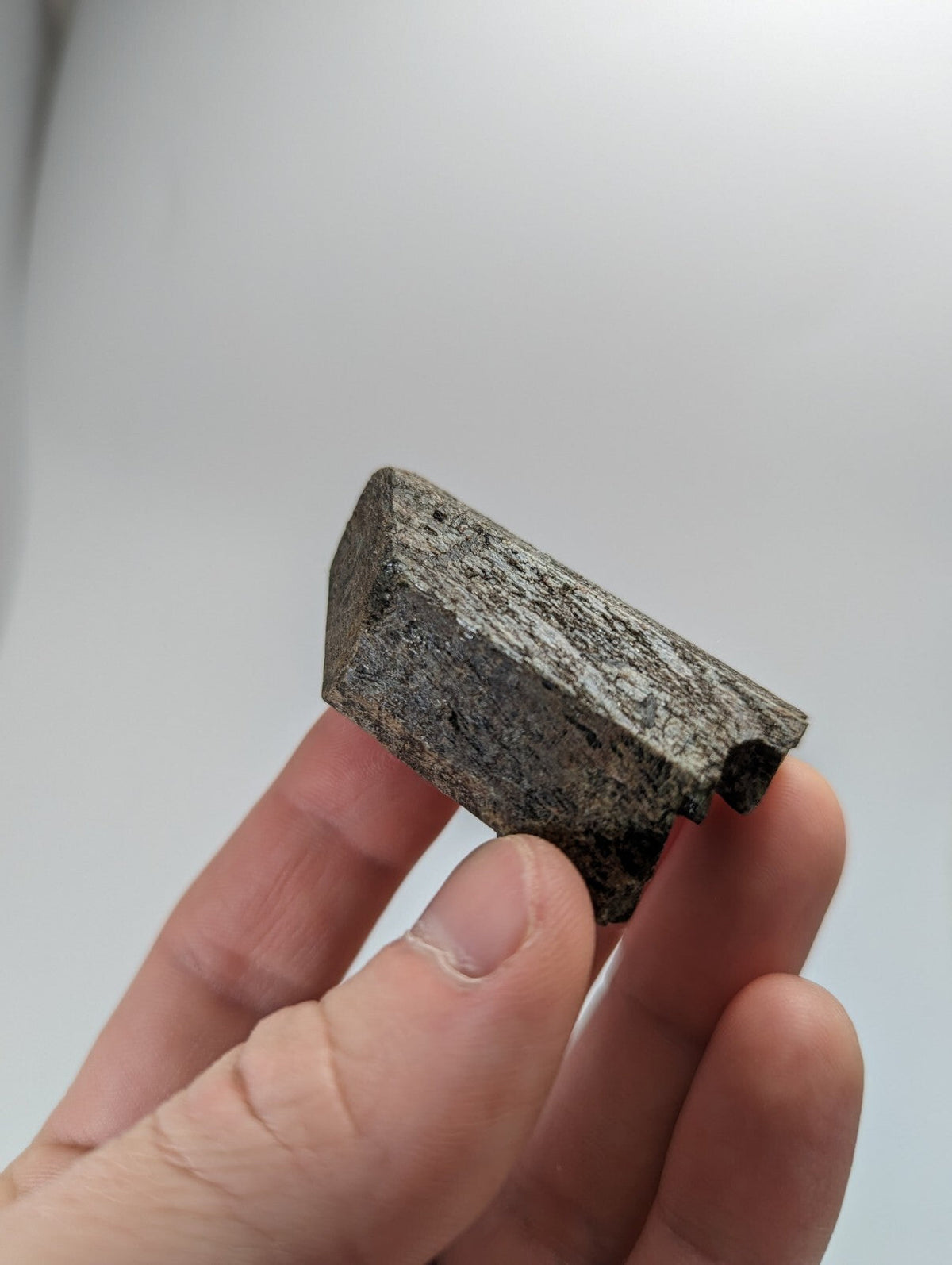 A dark gray, rough-textured stone fragment with a jagged edge and uneven surface.