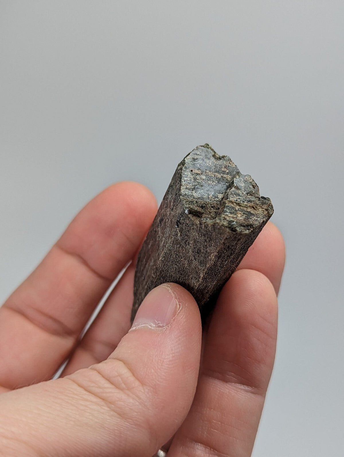 A dark, rough-textured mineral specimen with a jagged top and layered internal patterns.