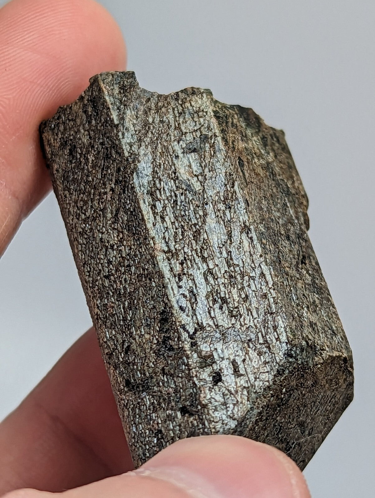 A rough, dark gray mineral specimen with a textured surface and visible crystalline patterns.