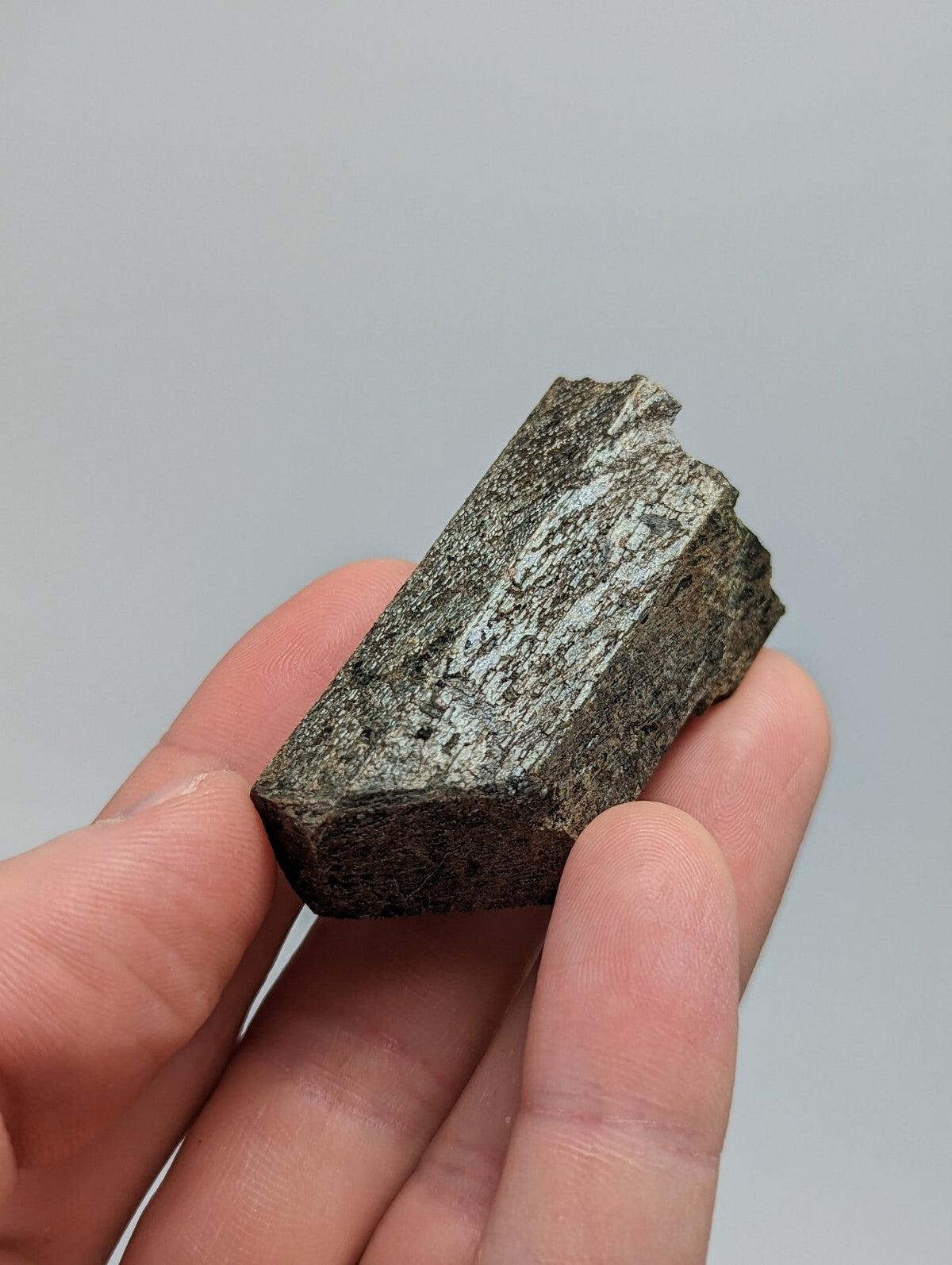 A dark, rough-textured mineral specimen with a metallic sheen and visible crystalline patterns.