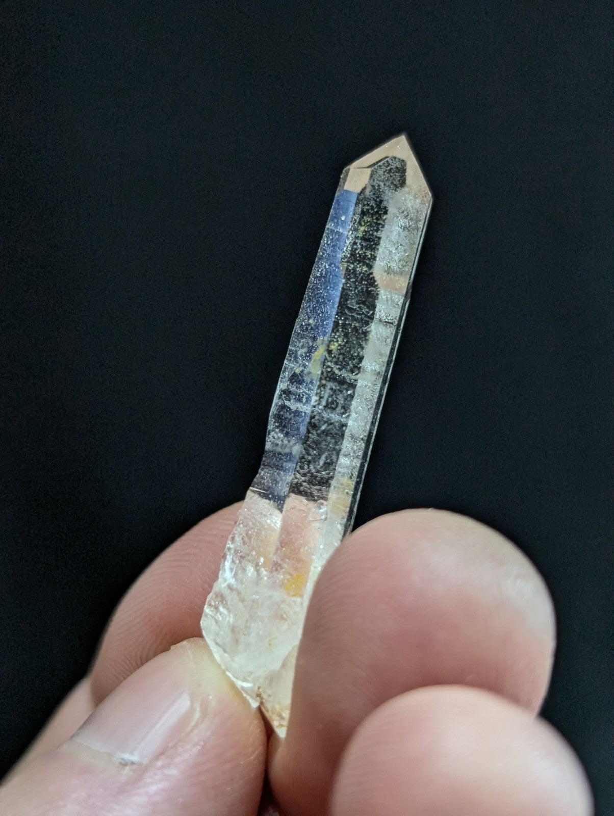 A translucent, clear quartz crystal with a pointed tip and natural inclusions of dark streaks and subtle blue hues.