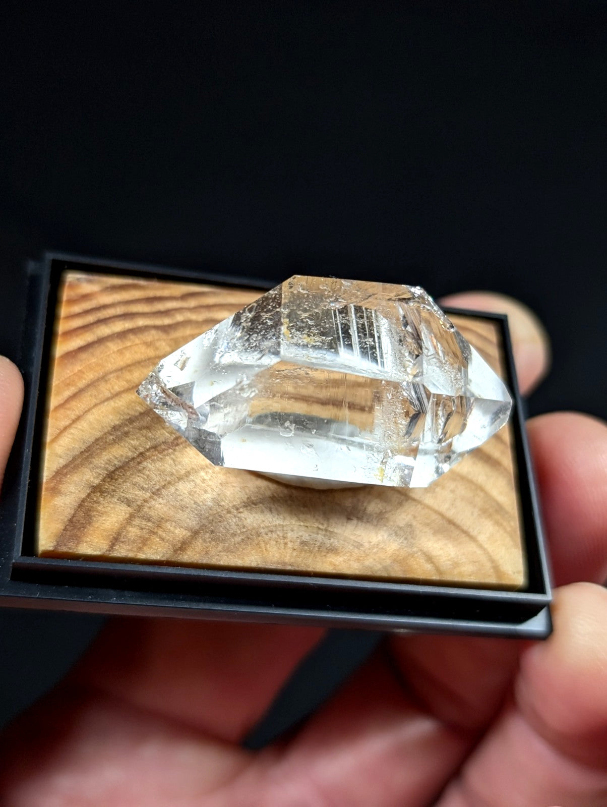 A clear, faceted quartz crystal with natural inclusions and a double-terminated shape rests on a wooden display base.